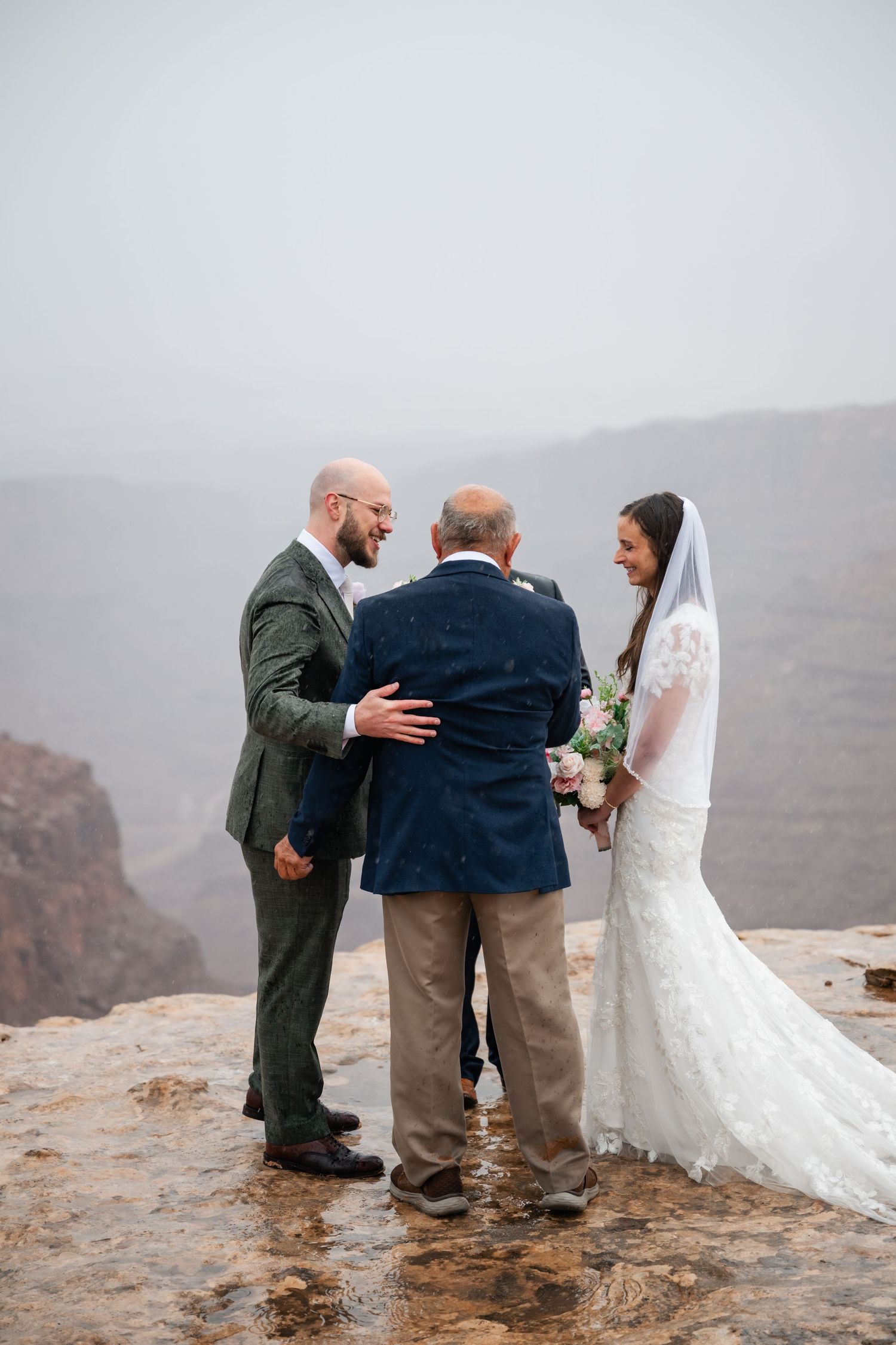 Wedding ceremony taking place on a dramatic cliffside overlook with misty mountains in the background.