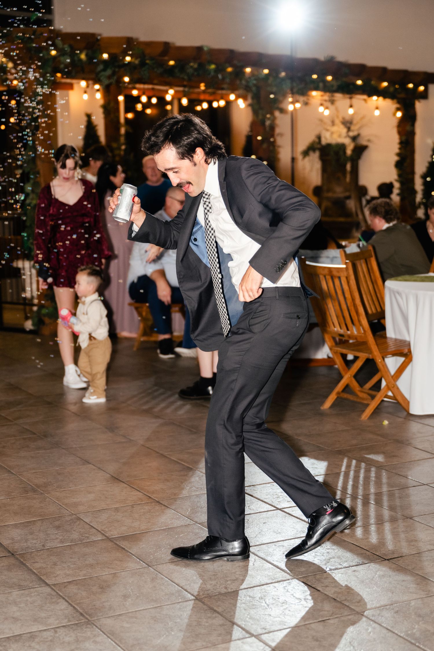 A man in a formal suit shows off energetic dance moves on a tiled floor at an elegant venue.
