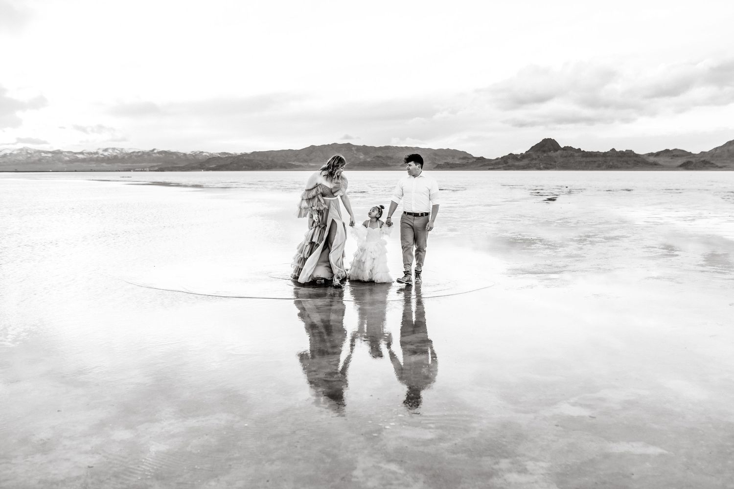 Family holding hands walking together through the lightly flooded Utah Salt Flats.