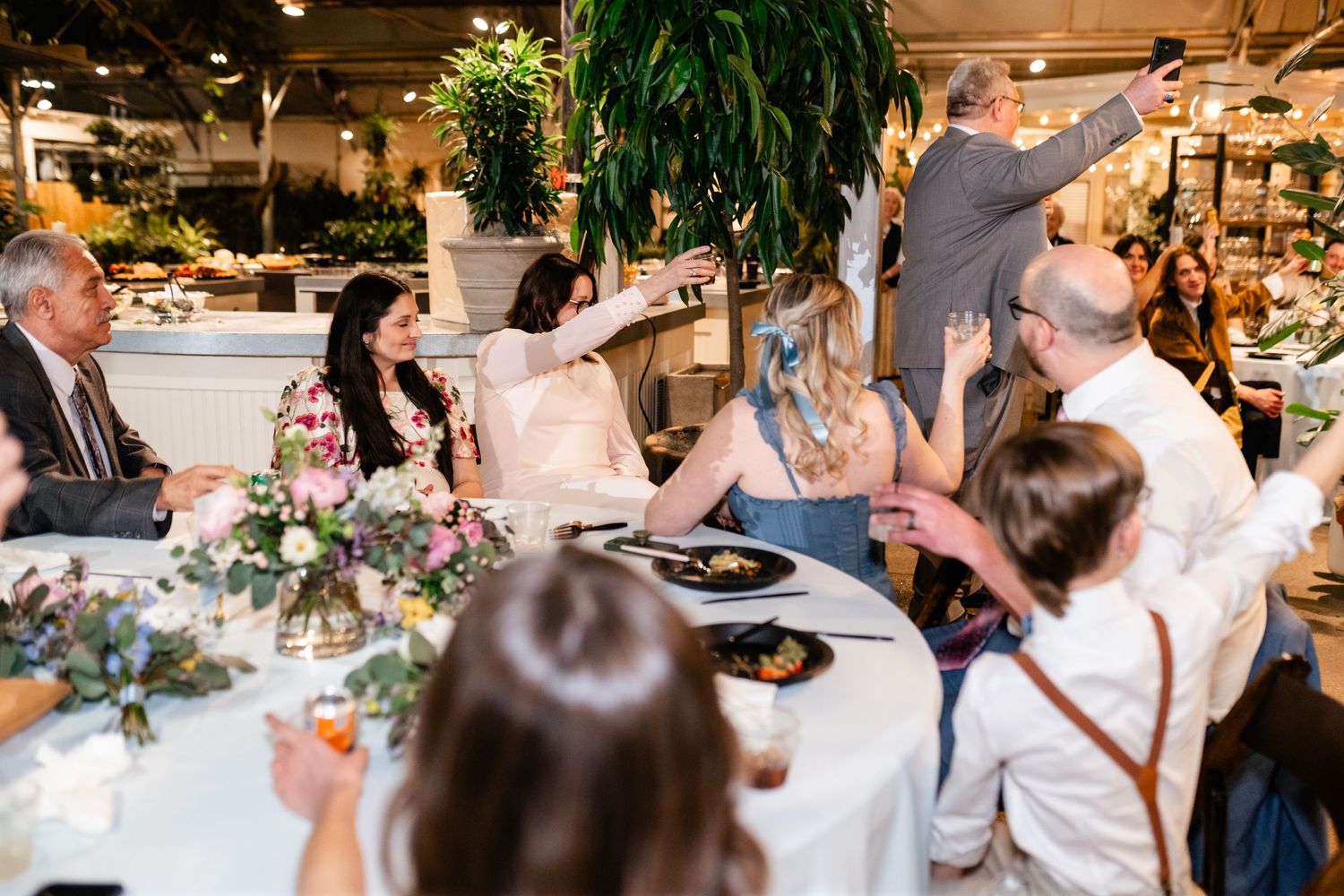 Dinner party guests enjoying an animated conversation around a decorated table with floral centerpieces at an indoor venue.