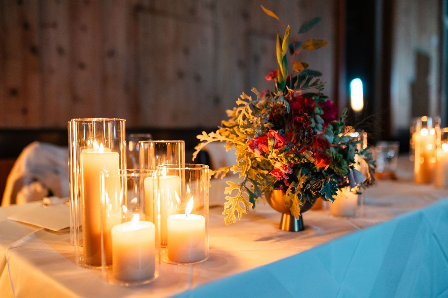 Glowing candles and autumn floral centerpiece arrangement on elegant table setting with blue tablecloth. Utah Wedding Photographer.