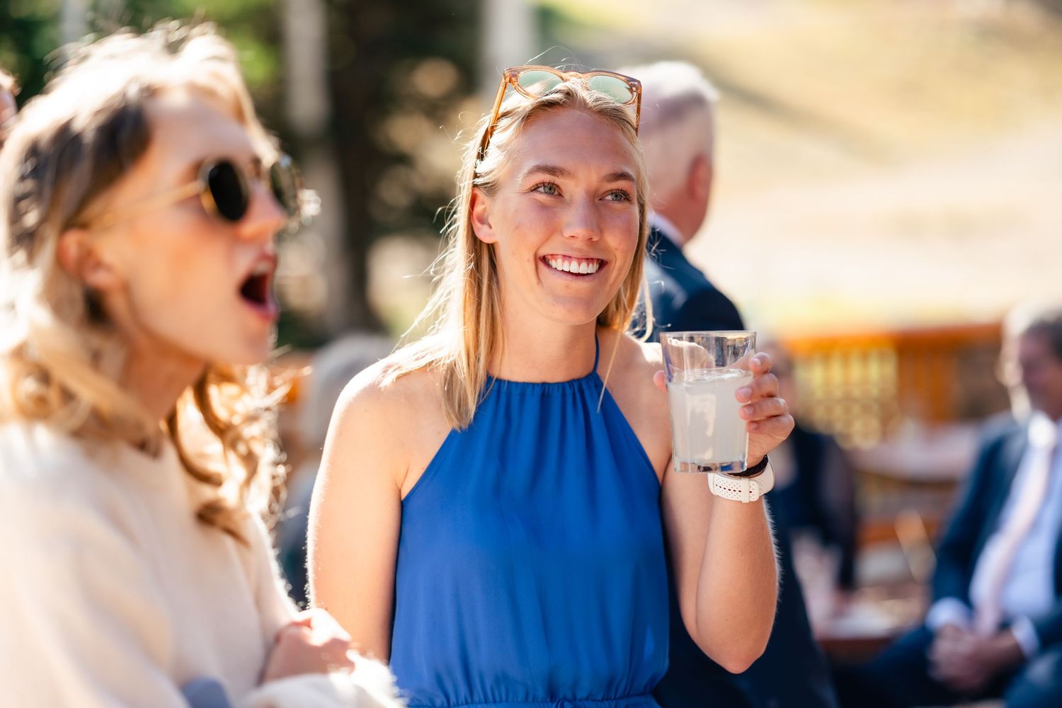 Person in bright blue halter dress smiling while holding cocktail at outdoor social gathering. Park City Wedding Photographer.