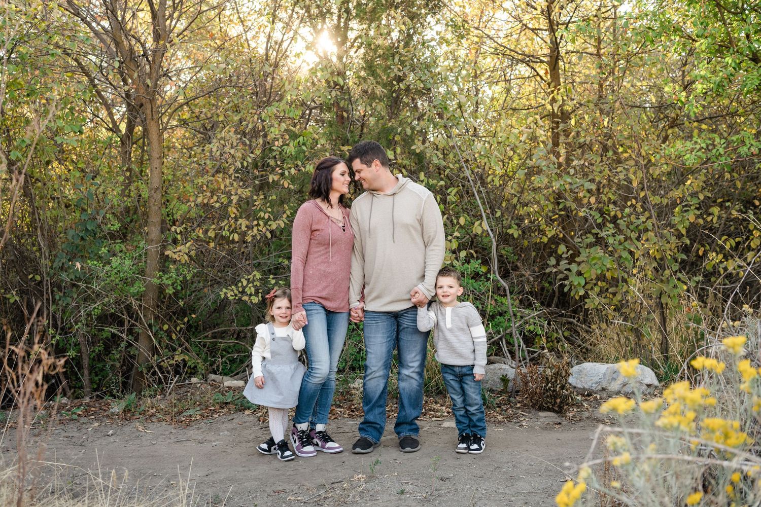 Family members stand together in a scenic outdoor setting with autumn foliage and golden sunlight filtering through trees.