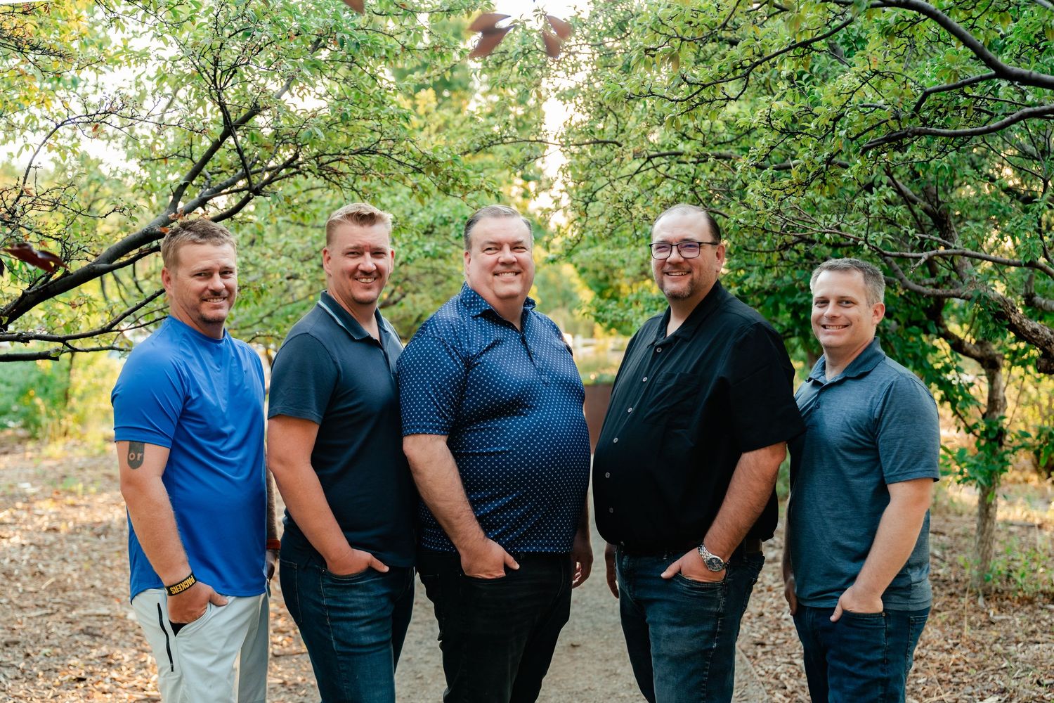 A group of people wearing blue and black shirts pose together outdoors in a casual setting.