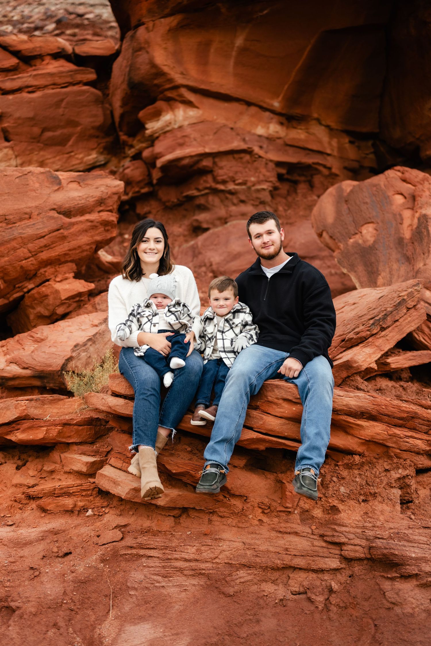 People relaxing on red rock ledges against a dramatic desert cliff backdrop.
