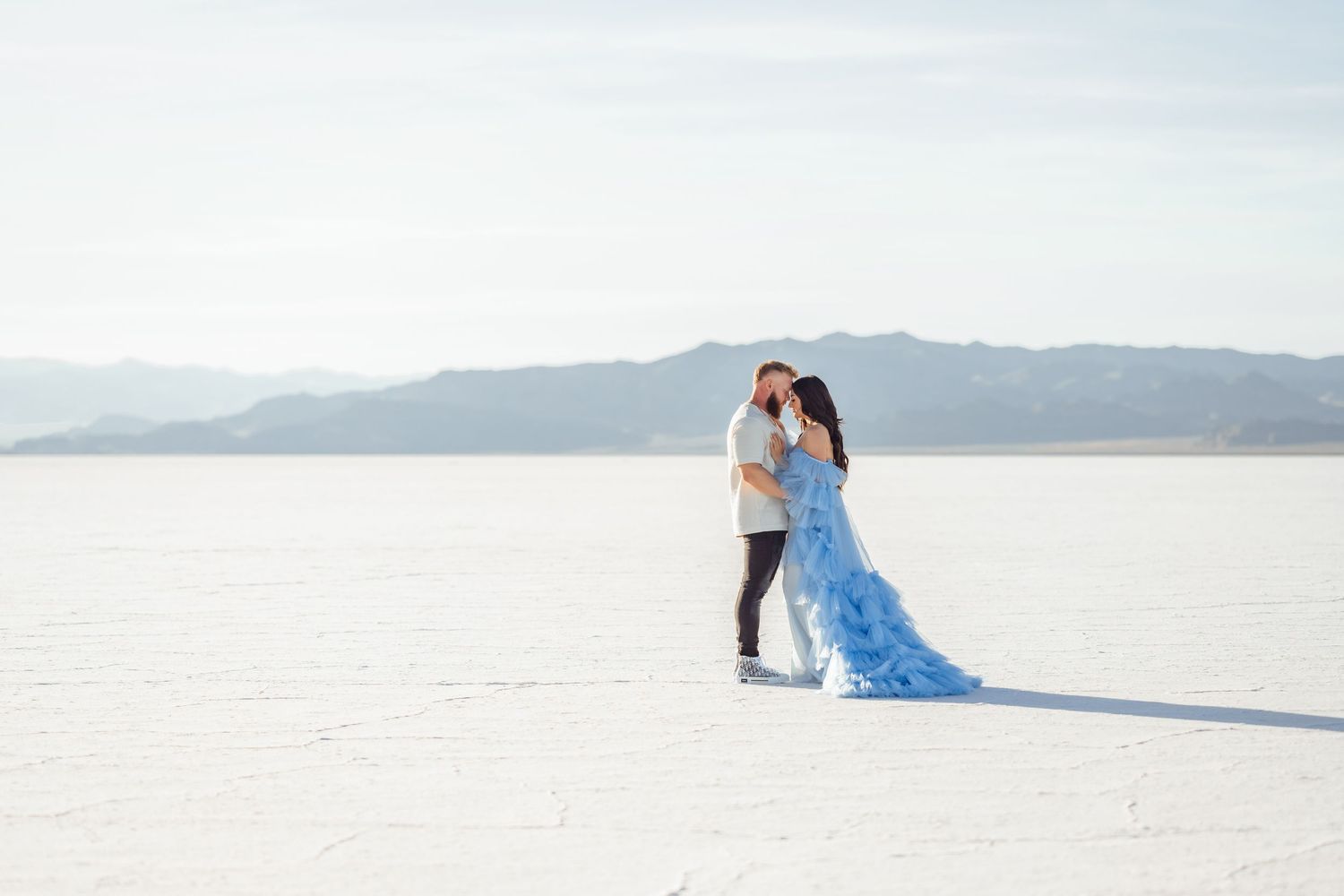 Utah Salt Flats Photographer. A couple in elegant attire poses against the stark white landscape of a salt flat during a photoshoot.