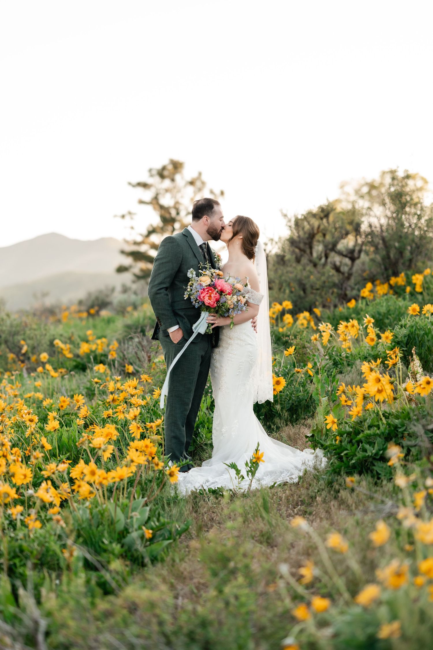 A romantic wedding couple shares a tender moment among vibrant yellow wildflowers in a scenic outdoor setting.