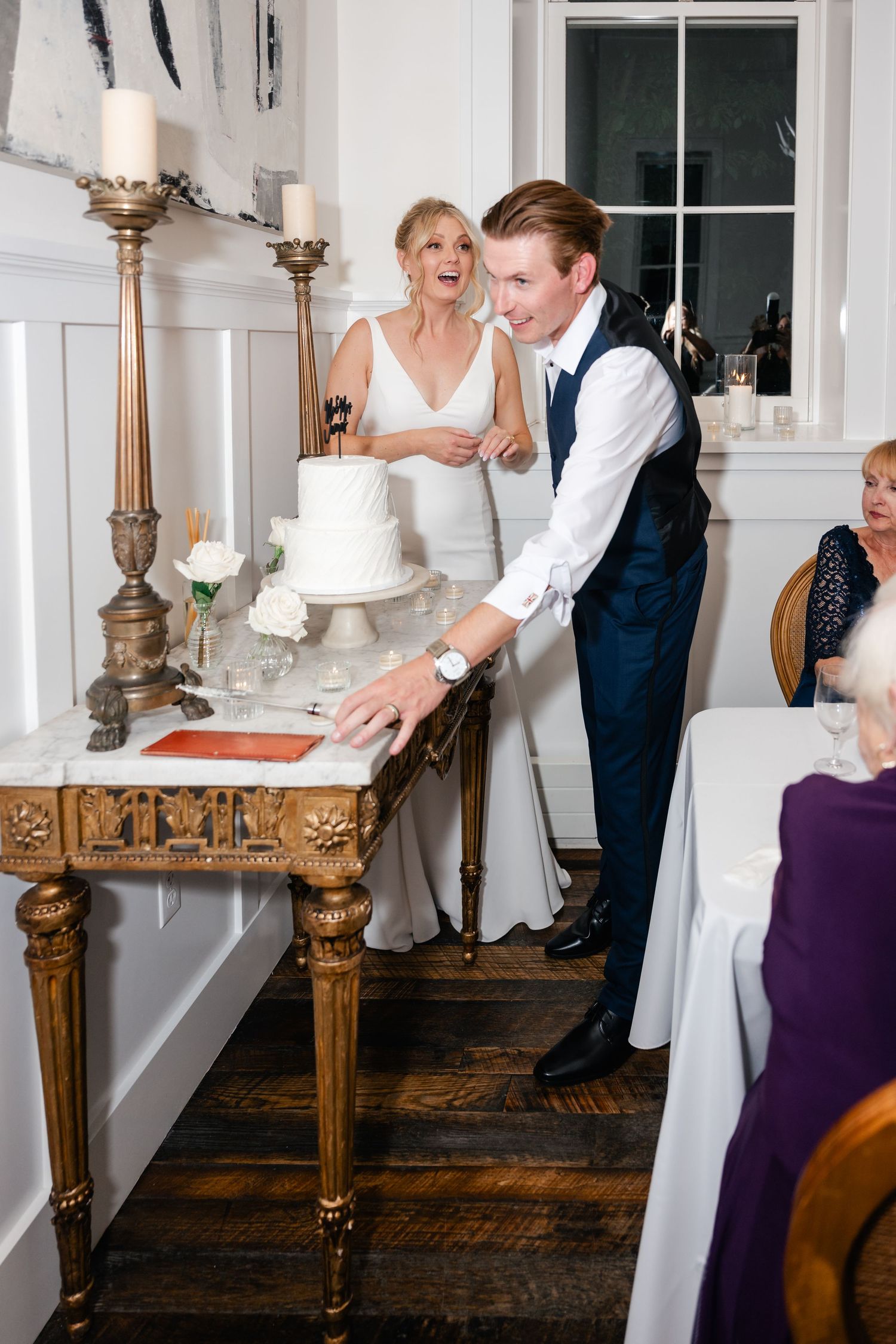 Playful wedding couple shares a fun moment with their cake at an elegant indoor reception venue.