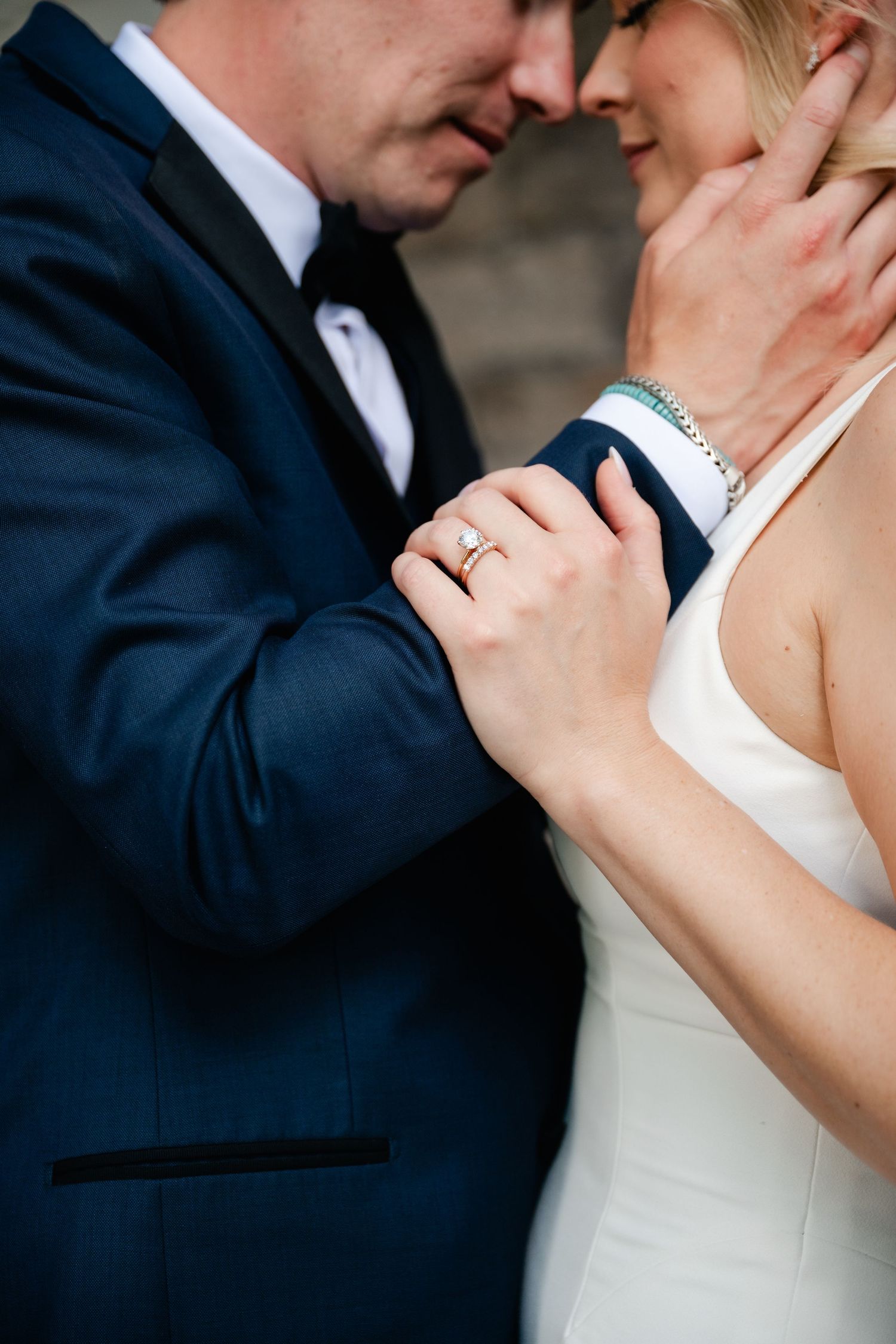 Close-up of wedding rings and tender embrace showing white dress and navy suit details.