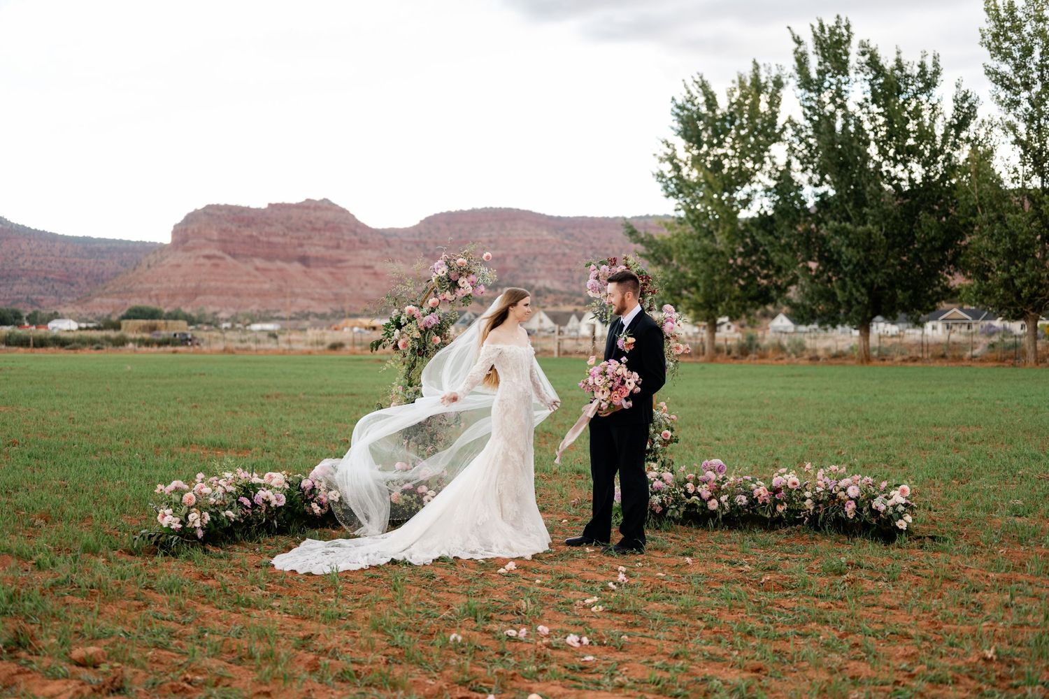 A romantic wedding couple poses against the backdrop of red rock formations in a desert landscape. Best Utah Wedding Photographers.