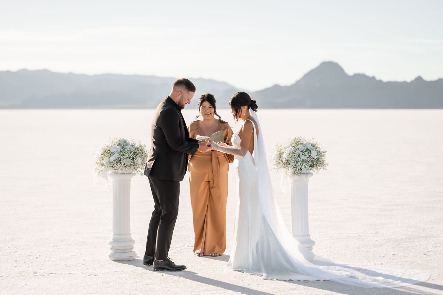 Wedding ceremony setup on vast white salt flats with mountains in background.