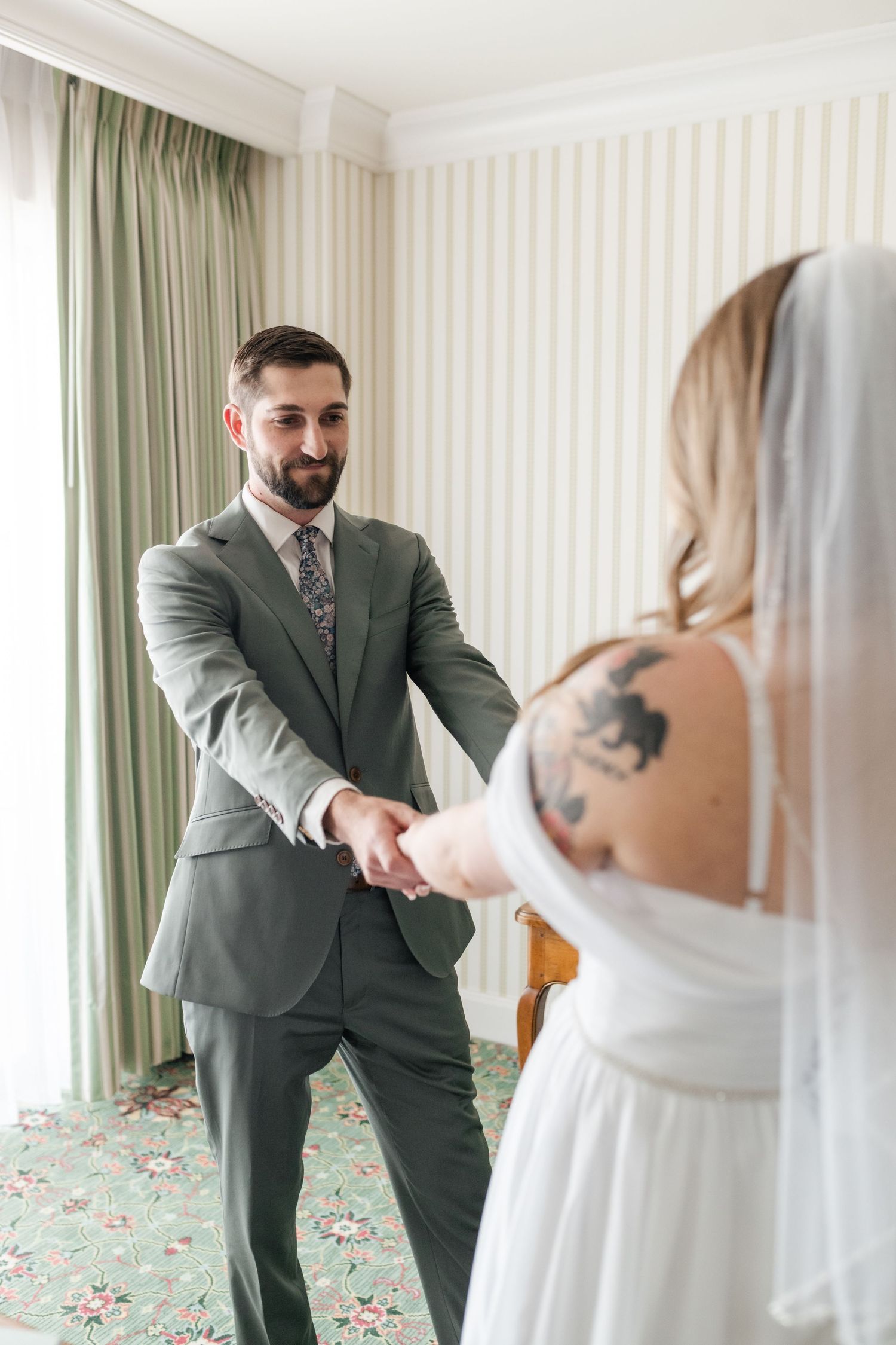 Wedding first look moment captured in a room with striped wallpaper and green curtains.