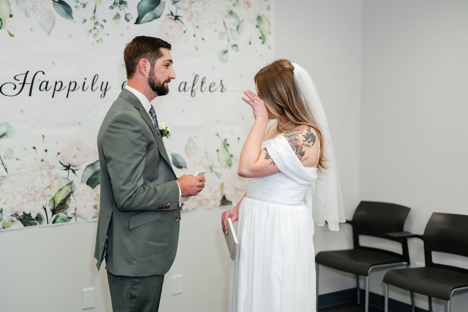 A couple interacts during their first look wedding moment against a white wall with botanical prints.