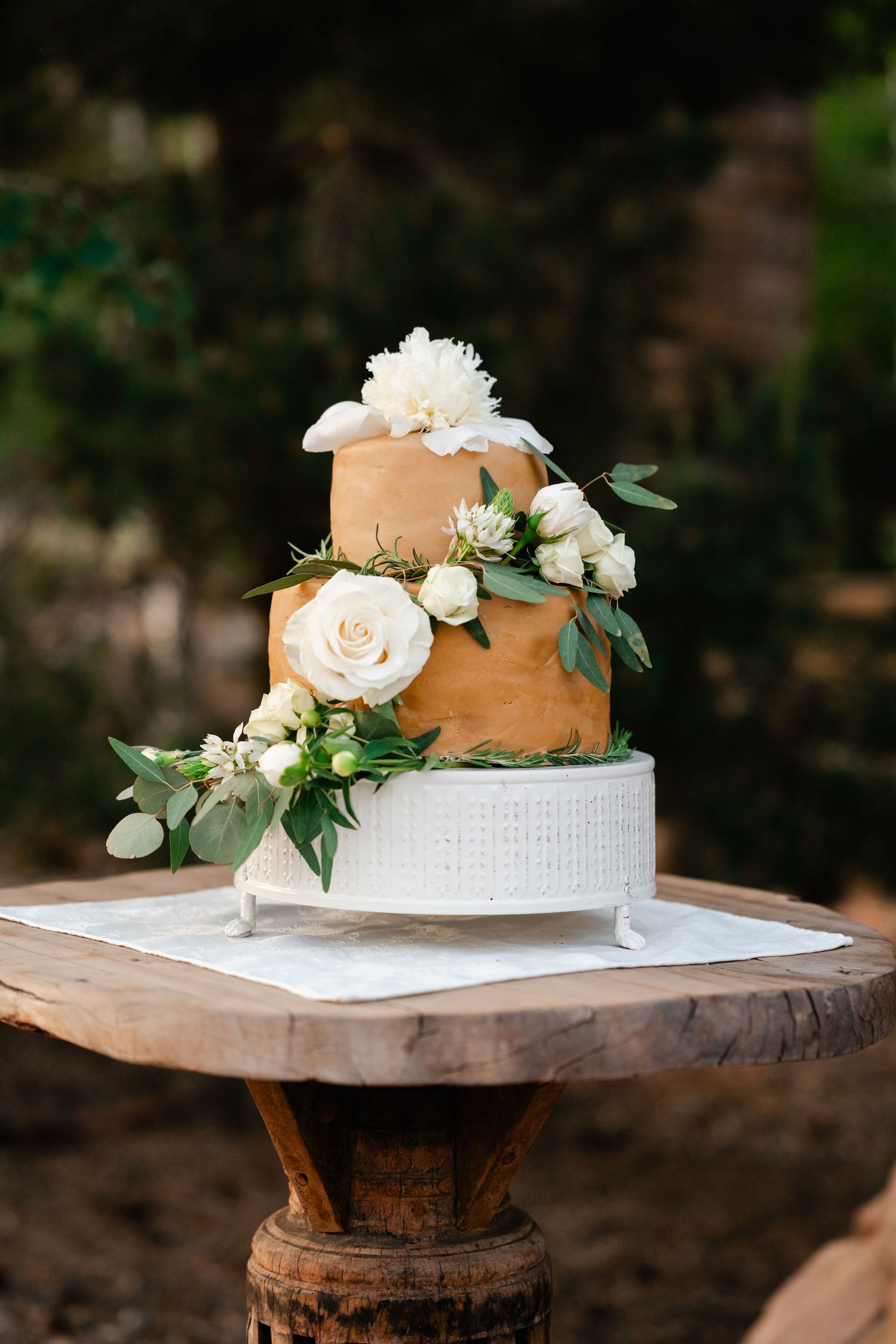 Wedding cake decorated with white roses and greenery displayed on wooden stands.