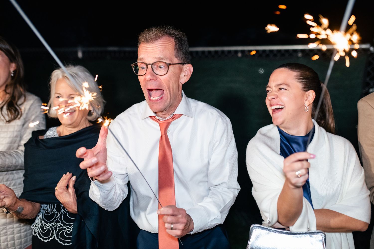 Wedding guests celebrating with sparklers at nighttime reception.