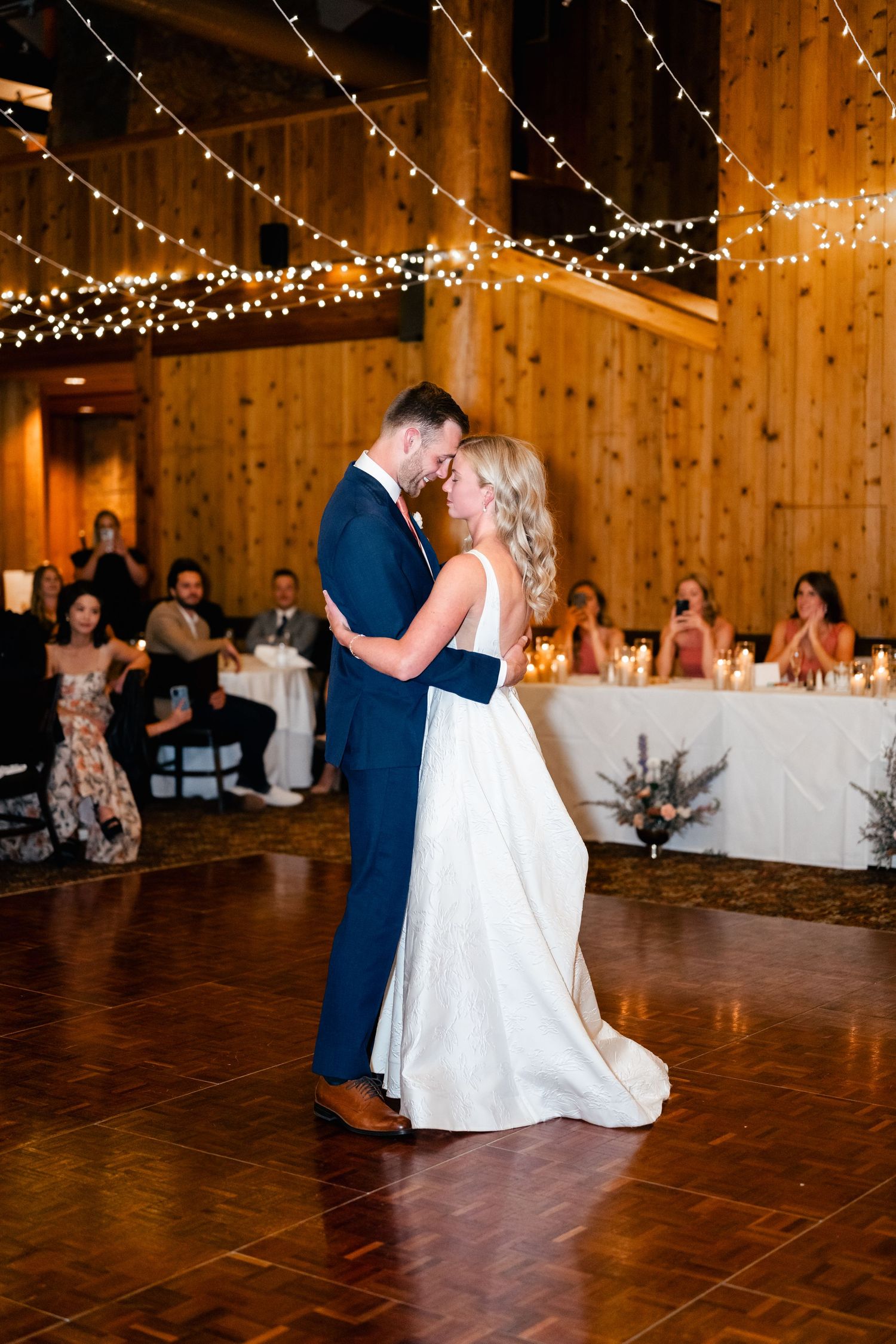 Wedding celebration in a wooden barn venue with string lights and white tablecloths creating an elegant atmosphere.