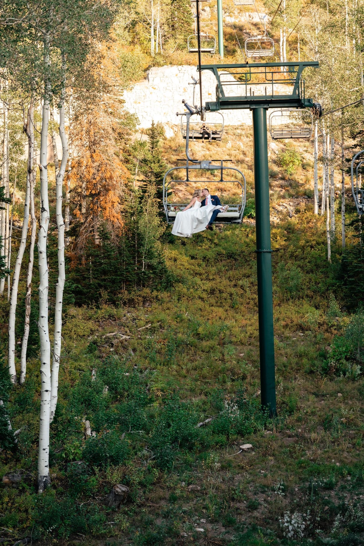 Empty ski lift chairs suspended above a mountainside with aspen and pine trees in summer.