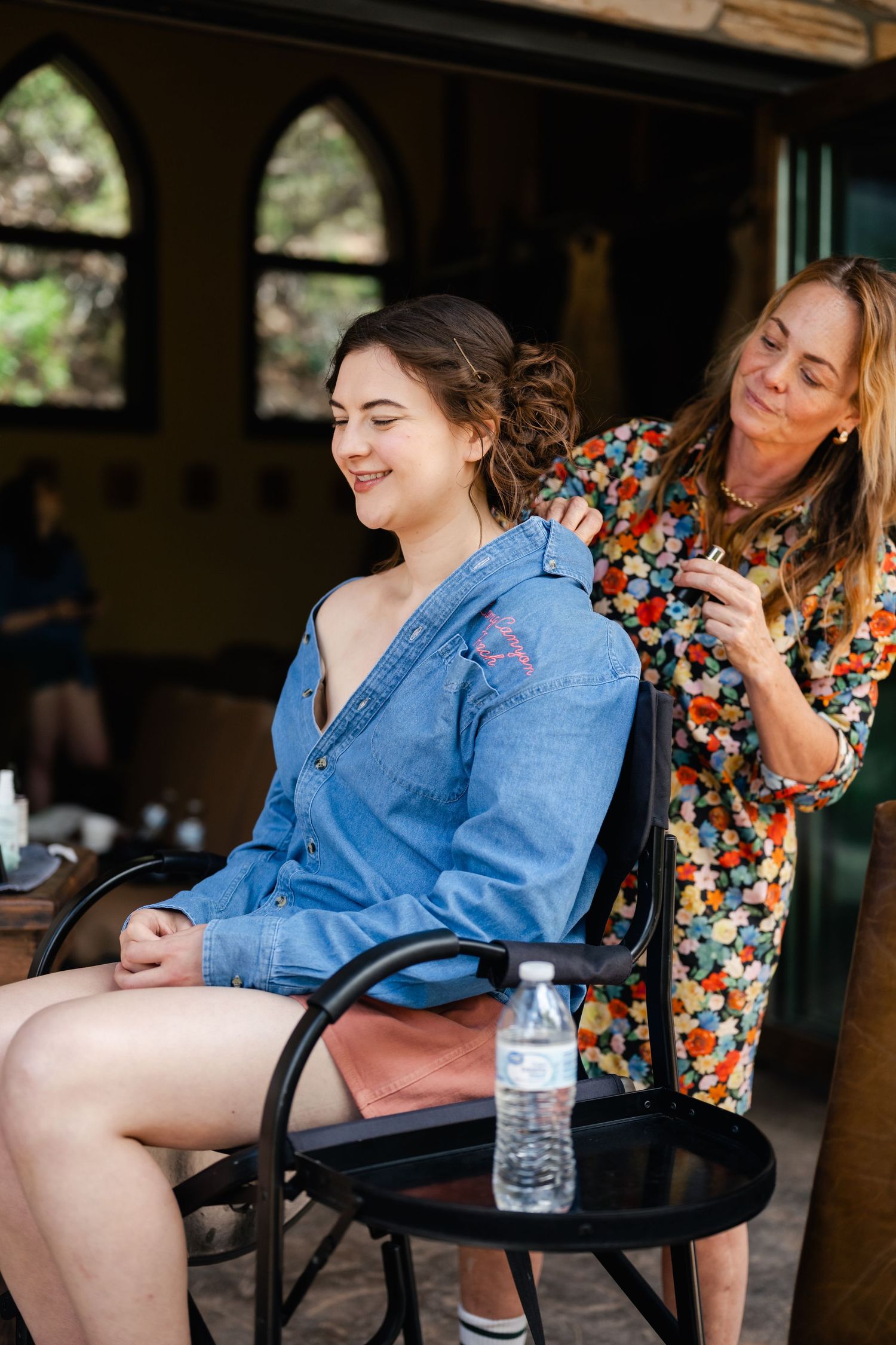A person in denim sitting in a chair getting their hair styled before a special event.