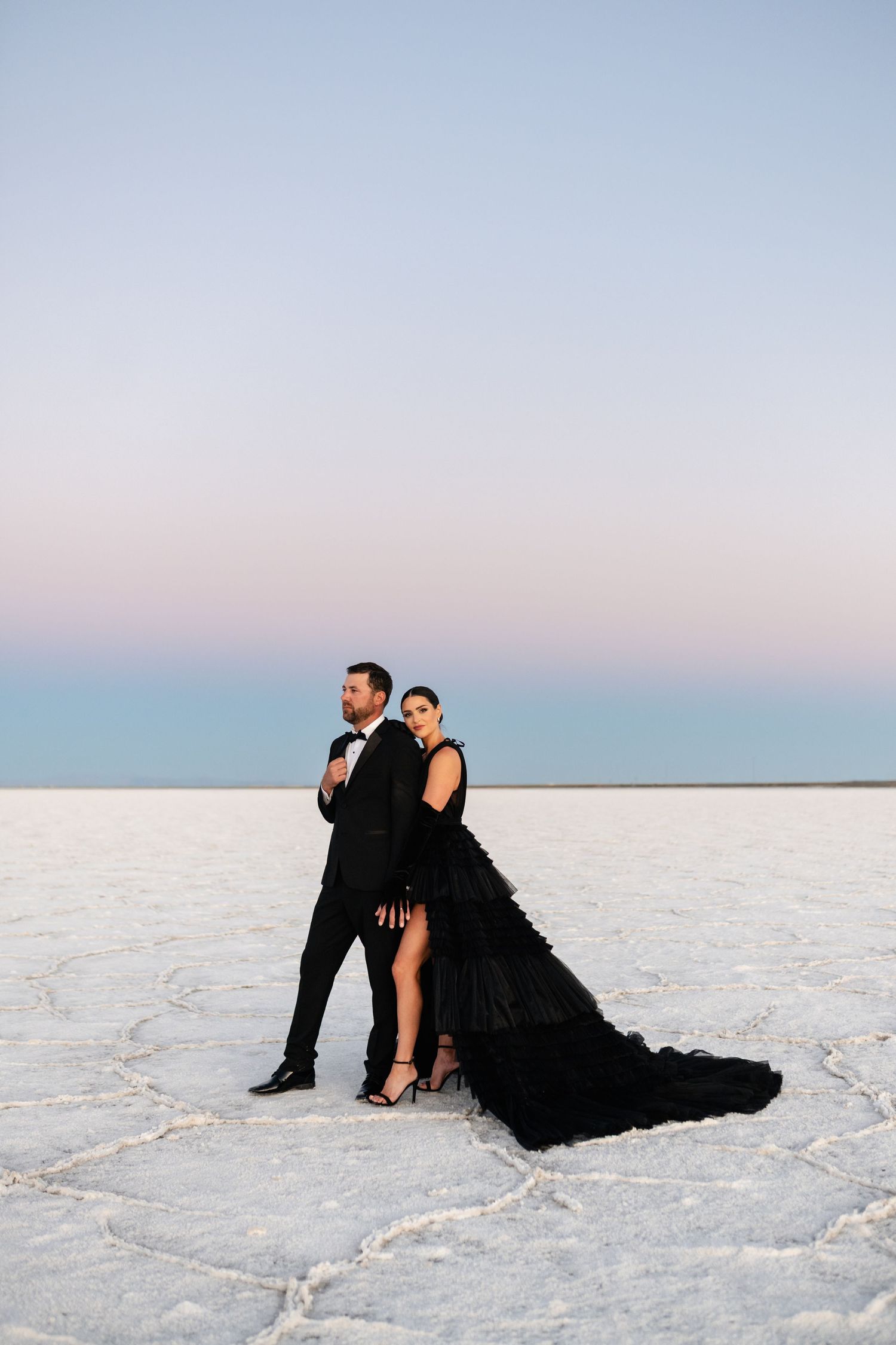 A romantic couple at white salt flats at sunset wearing formal black attire against a pastel sky at the Salt Flats. Salt Flats Photographer