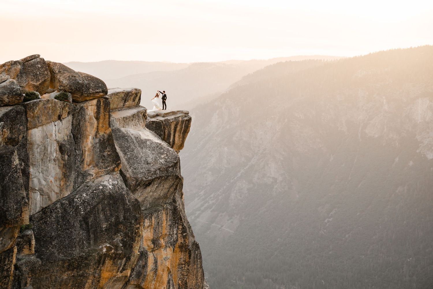 Couple standing on rocky cliff edge at Taft Point in Yosemite at sunset with mountain valley views.
