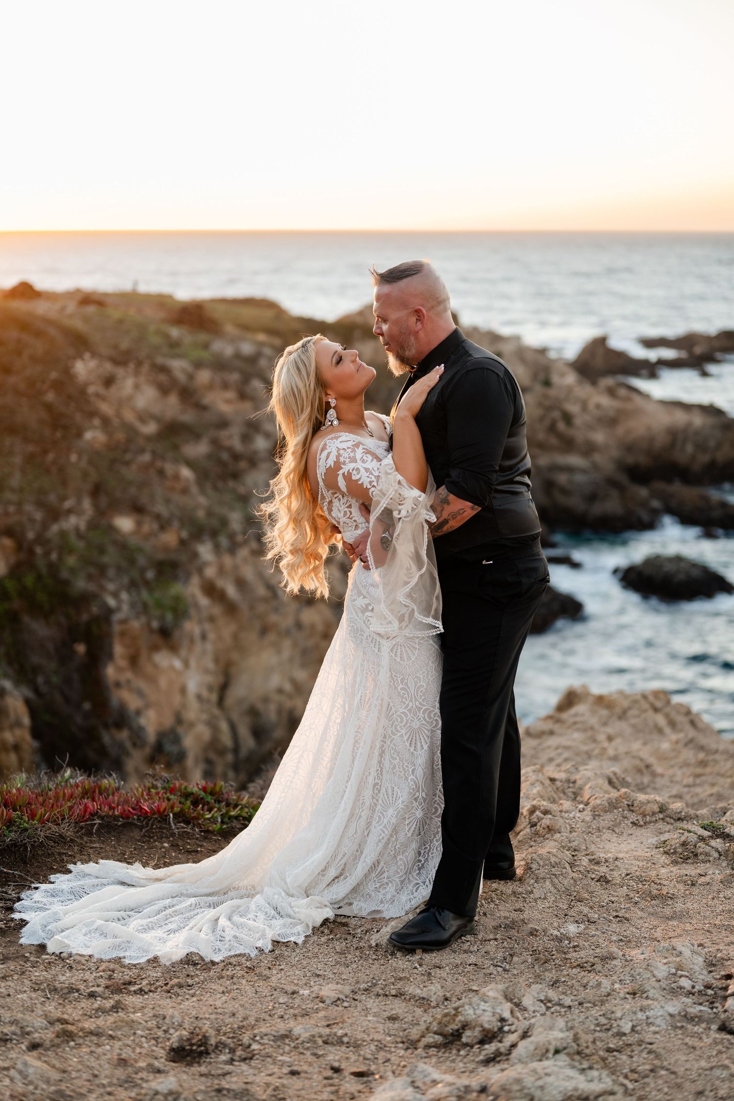A tender embrace between newlyweds against a dramatic ocean sunset backdrop.