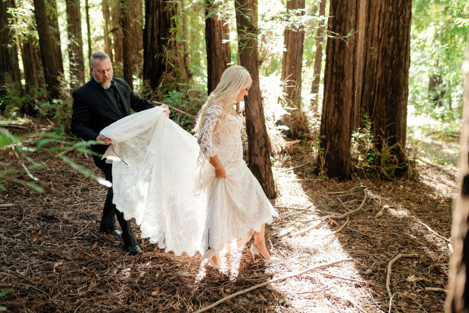 A couple poses for romantic wedding photos among towering redwood trees in a sunlit forest.