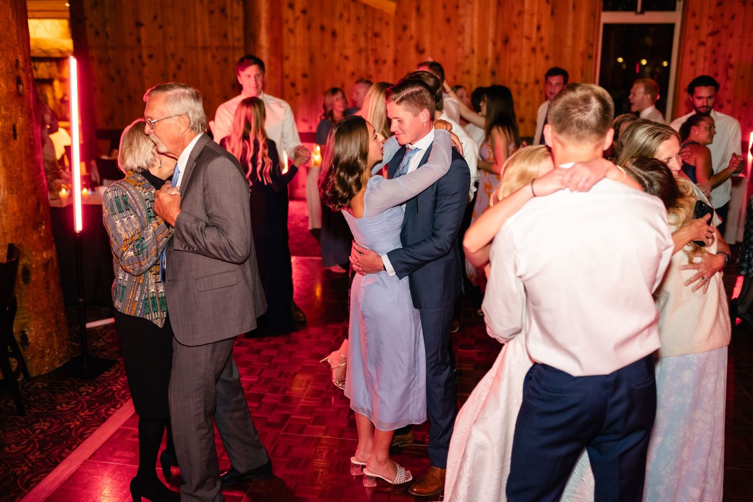 Couples slow dancing in a rustic barn venue illuminated by warm red lighting.