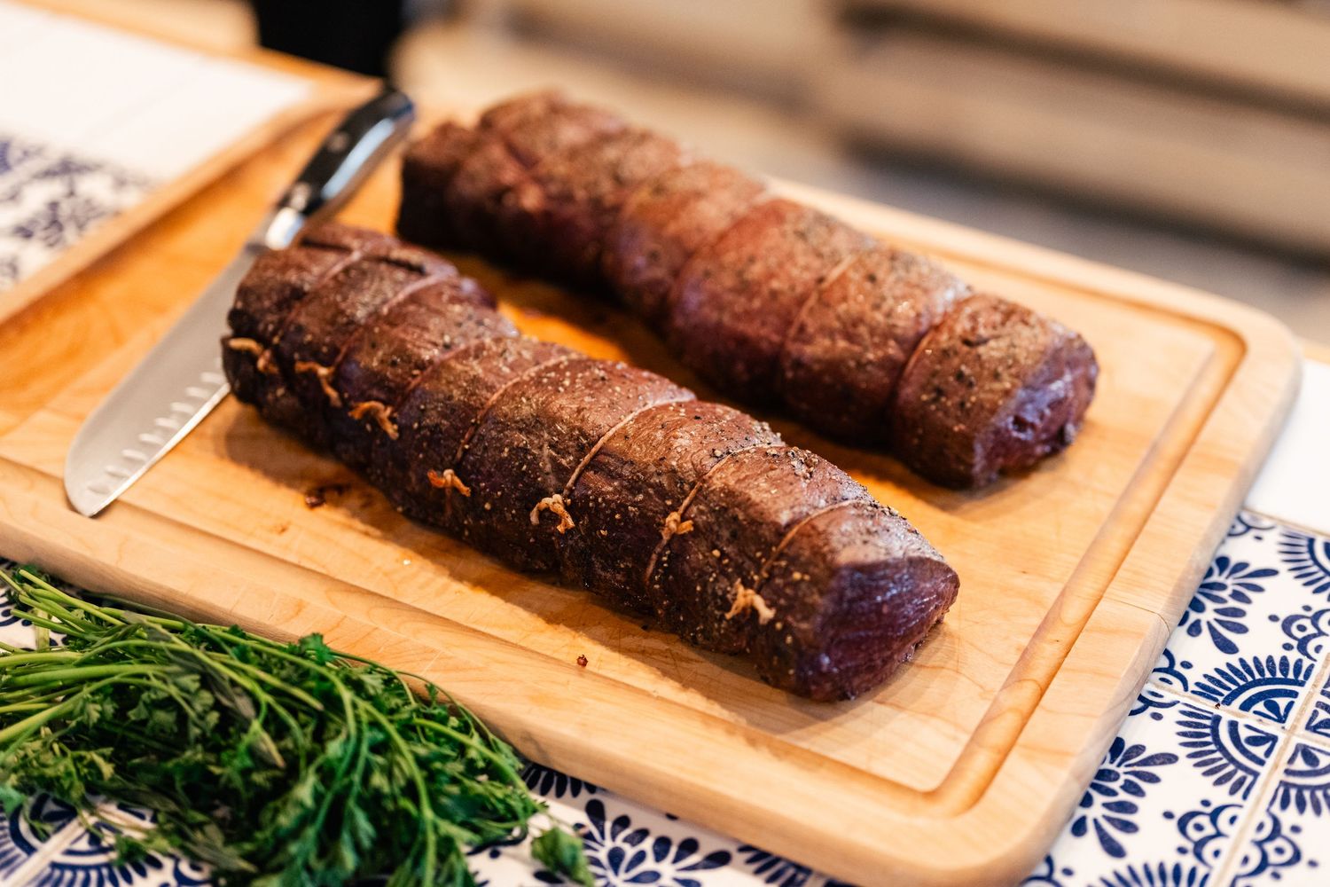 Dark chocolate dessert rolls arranged on a wooden serving board with fresh herbs.