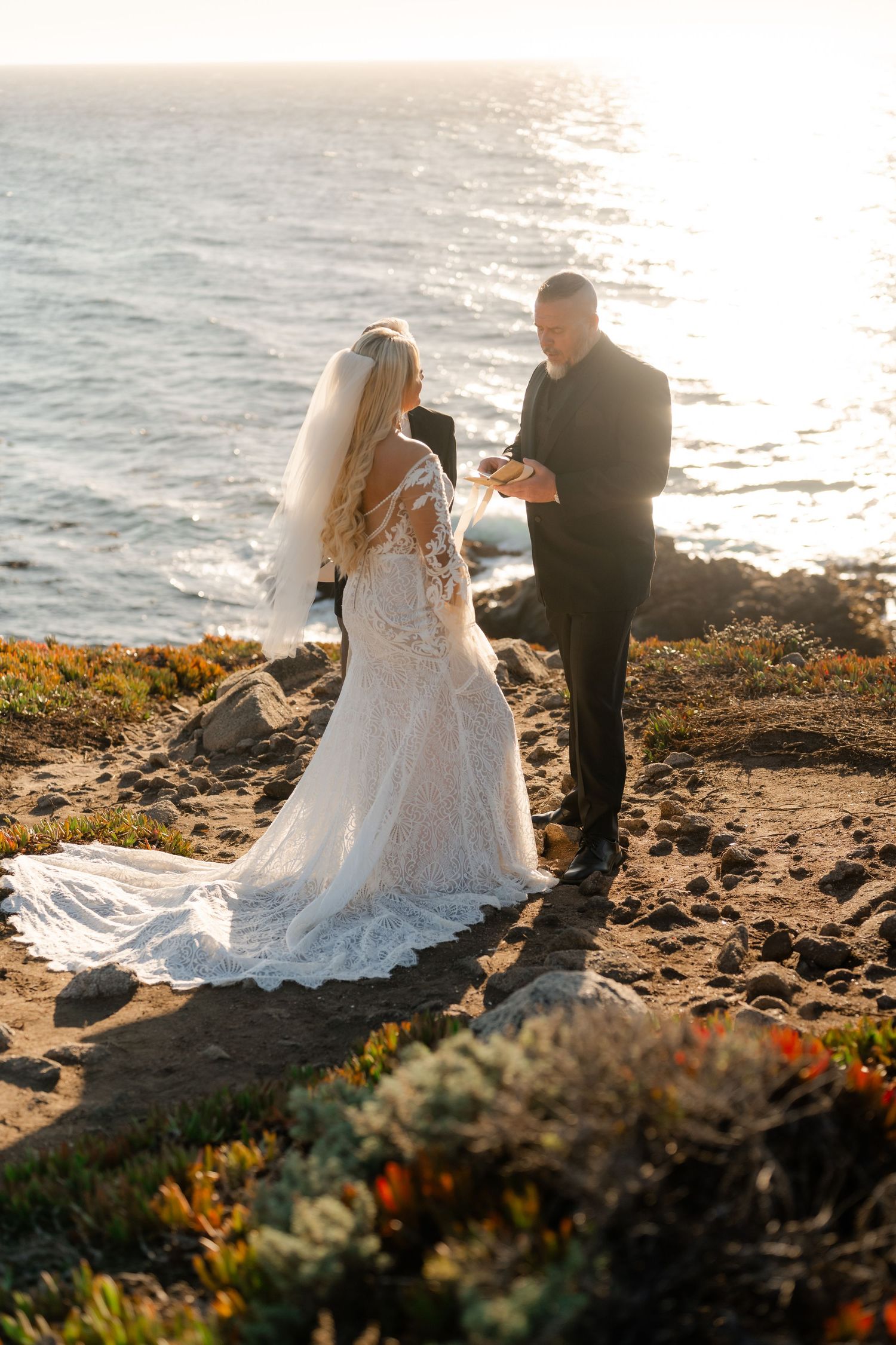 A couple shares an intimate moment during their sunset wedding ceremony on a coastal cliff overlooking the ocean.
