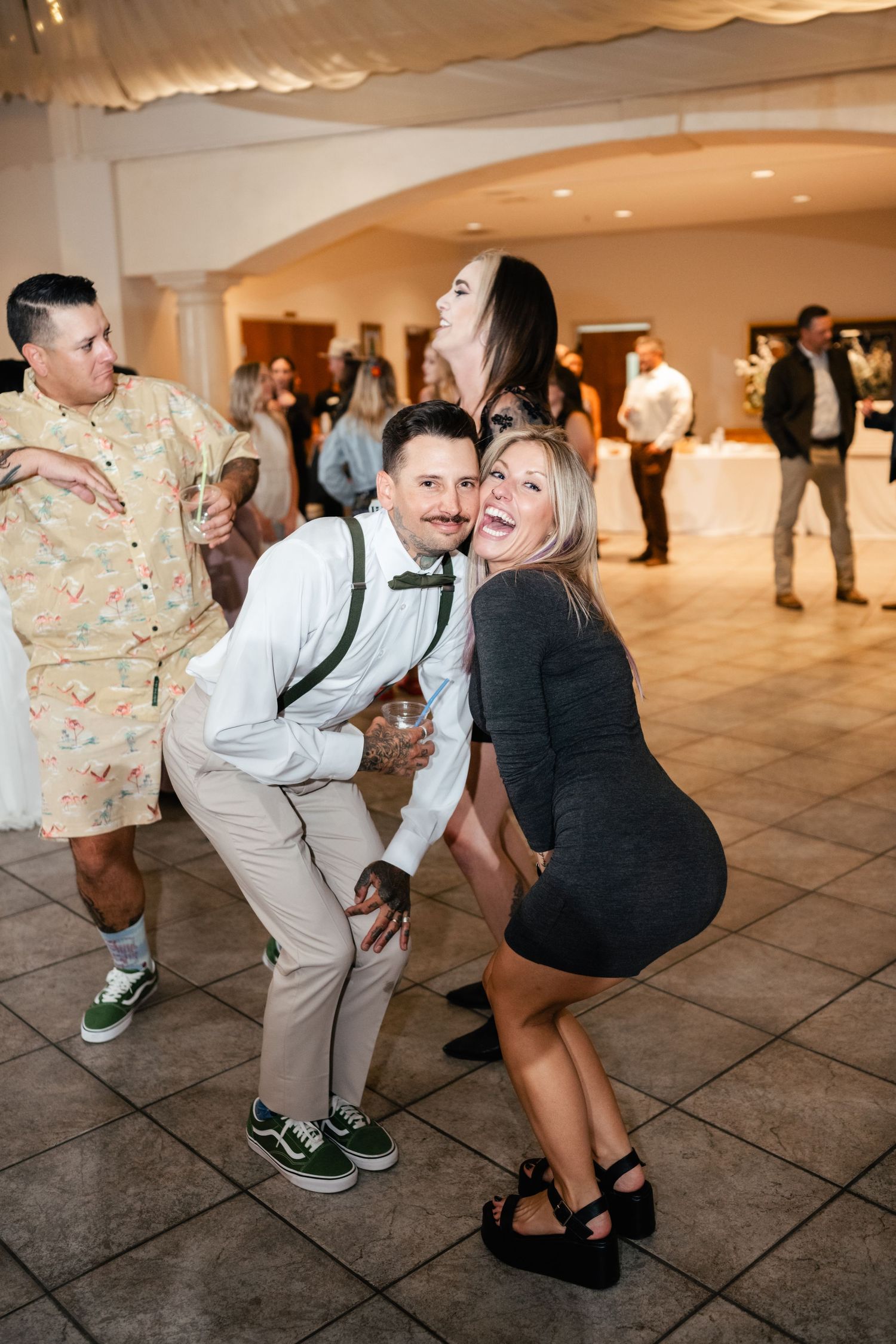 Wedding guests enjoying themselves and dancing on a tiled floor during a reception celebration.