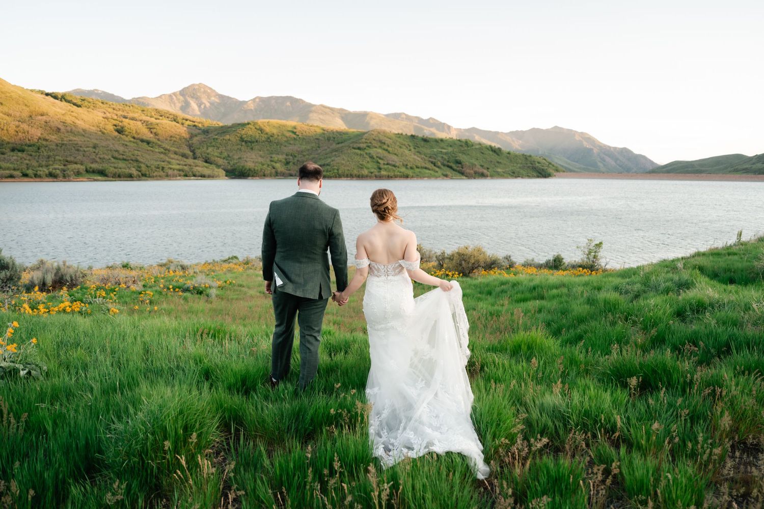Bride and groom stand together overlooking serene mountain lake and green hillsides.