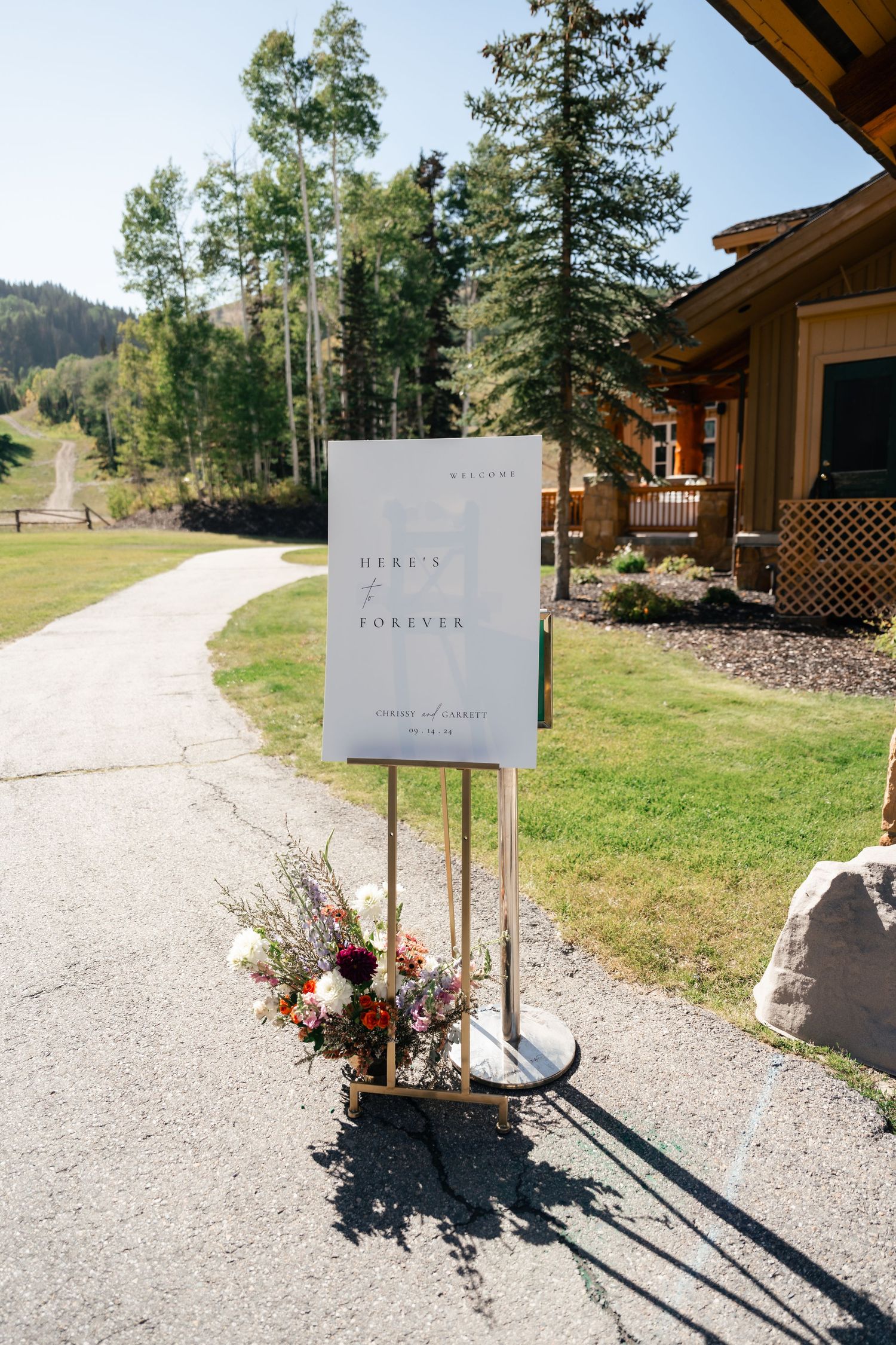 Wedding welcome sign displayed on stand with mountain backdrop and floral arrangement. Park City Wedding Photographer.