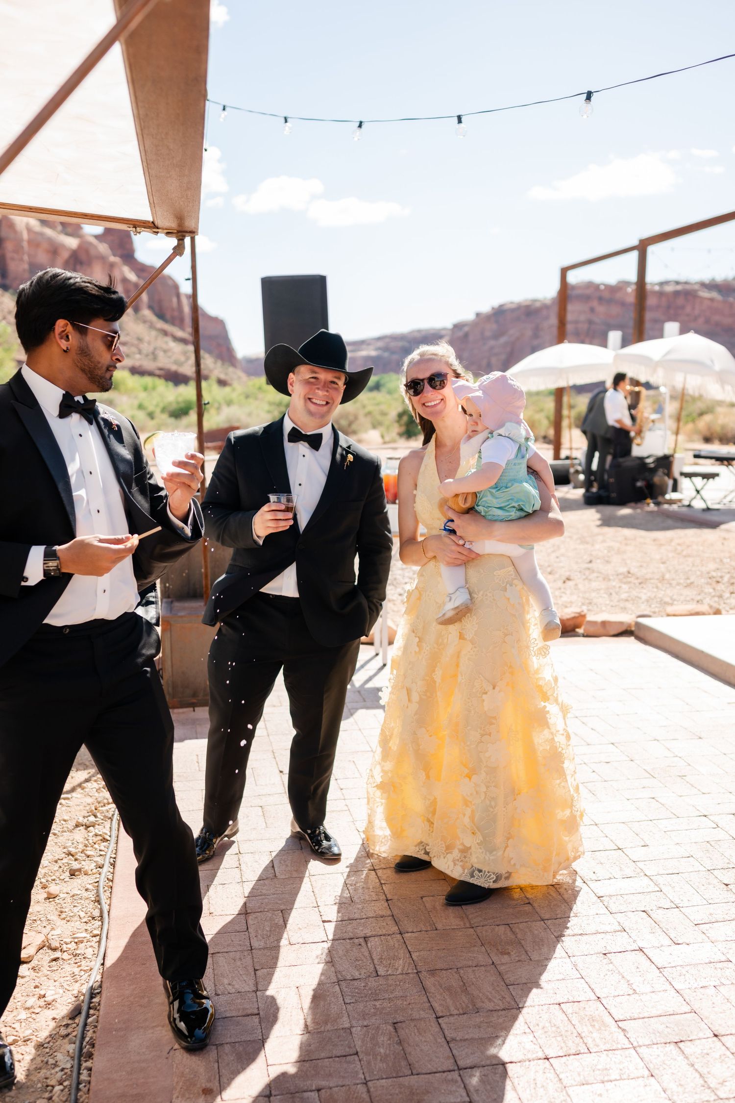 Wedding guests in formal attire, including tuxedos and a yellow gown, celebrate outdoors near red rock canyon scenery.