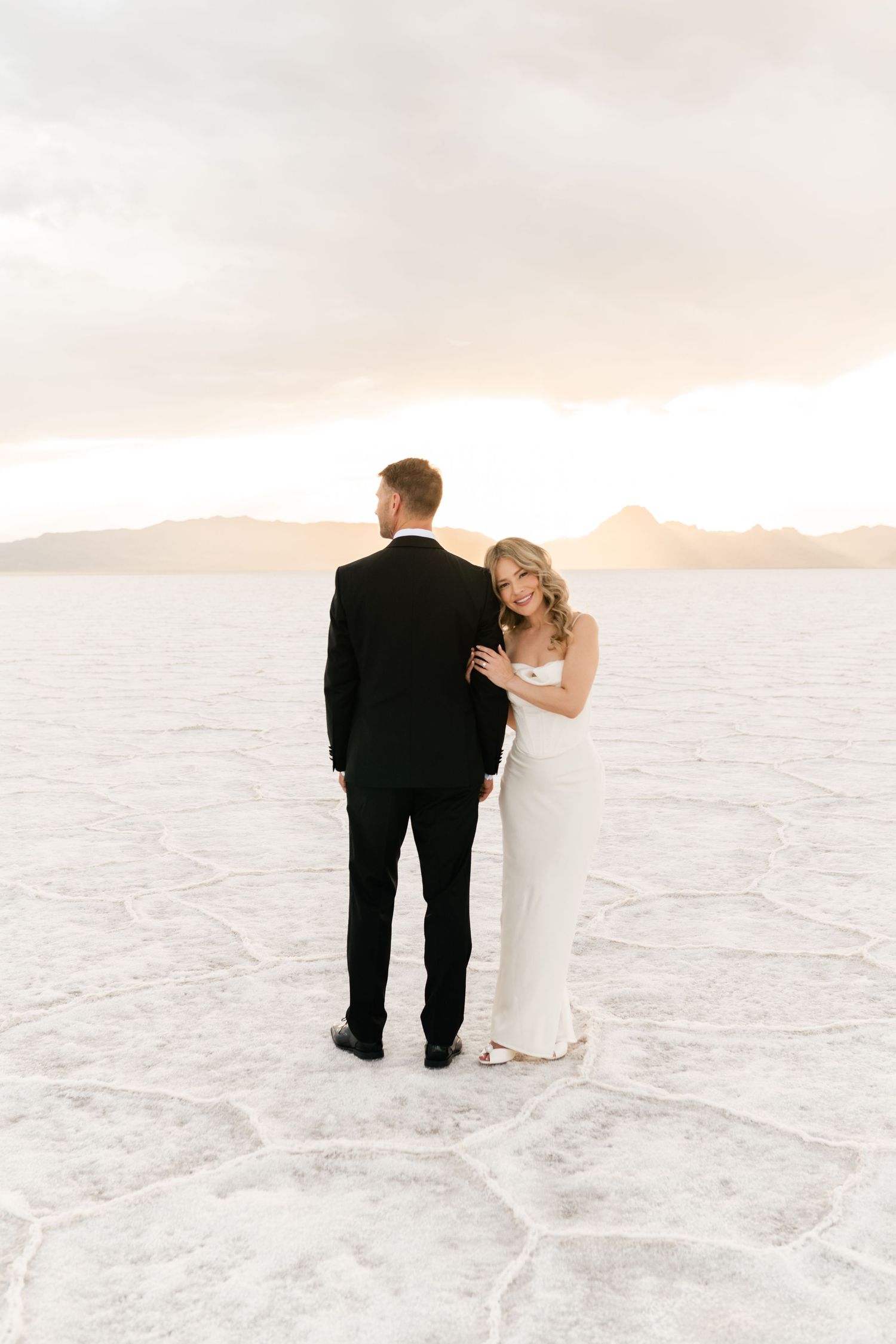 Salt Flats Elopement Photographer. A romantic couple in wedding attire stands on salt flats at sunset with mountains in the distance.