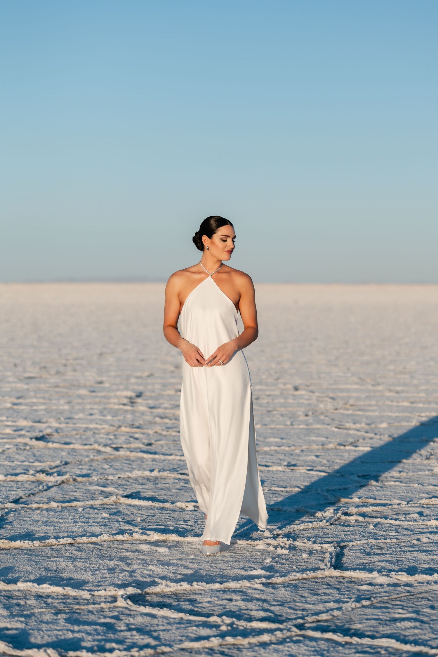 Salt Flats Photographer. A person draped in white fabric stands against the geometric patterns of a salt flat landscape.