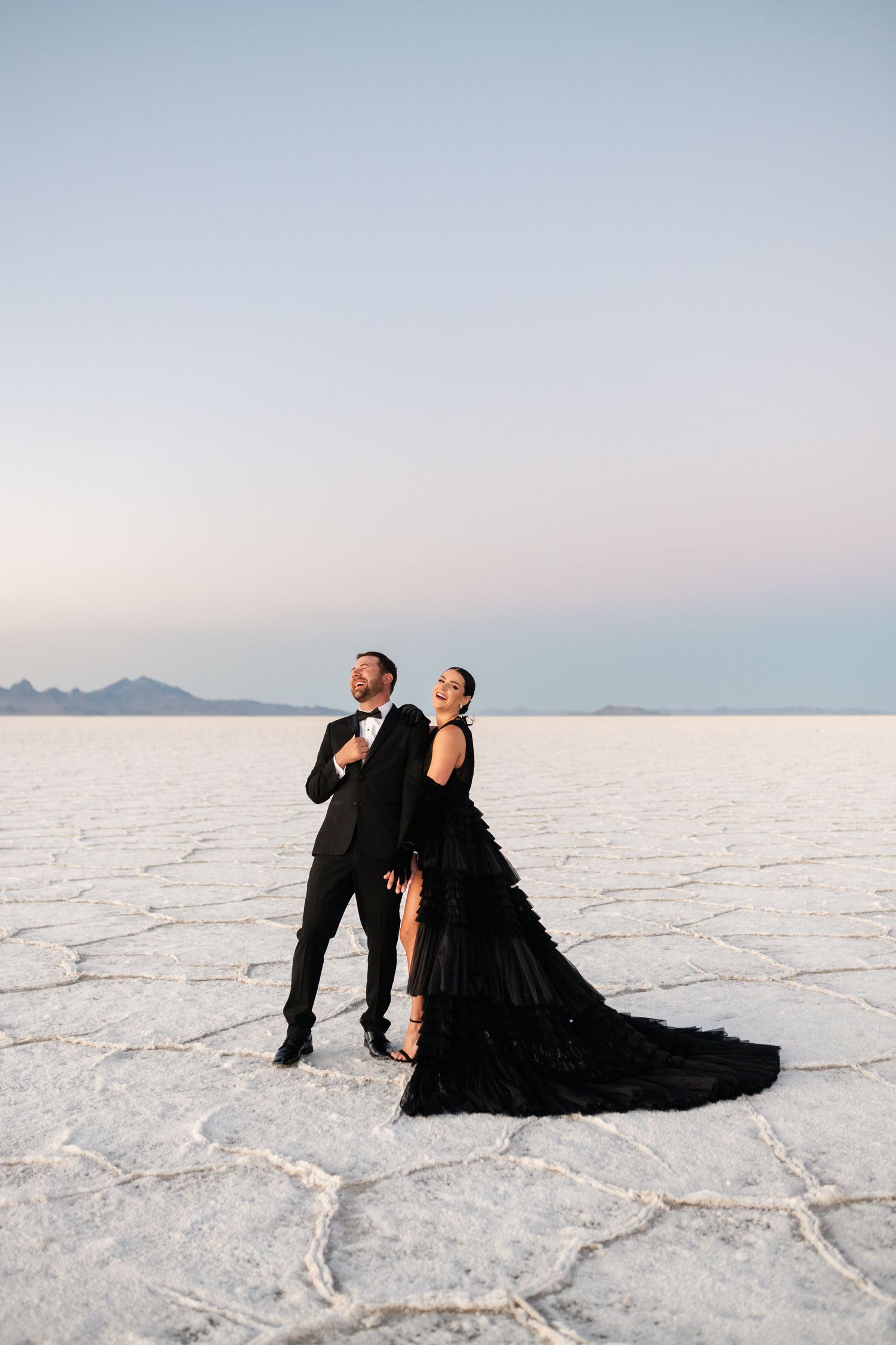 Utah Salt Flats Photographer. Stylish couple in black formal wear strike dramatic pose on salt flats at dusk.