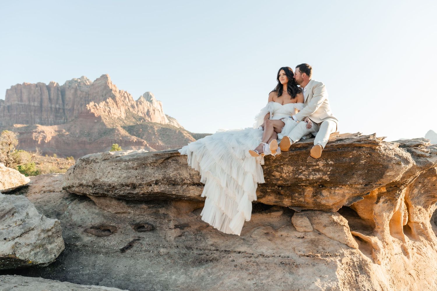 Couple sitting on rocky coastal cliffs at sunset overlooking the ocean.