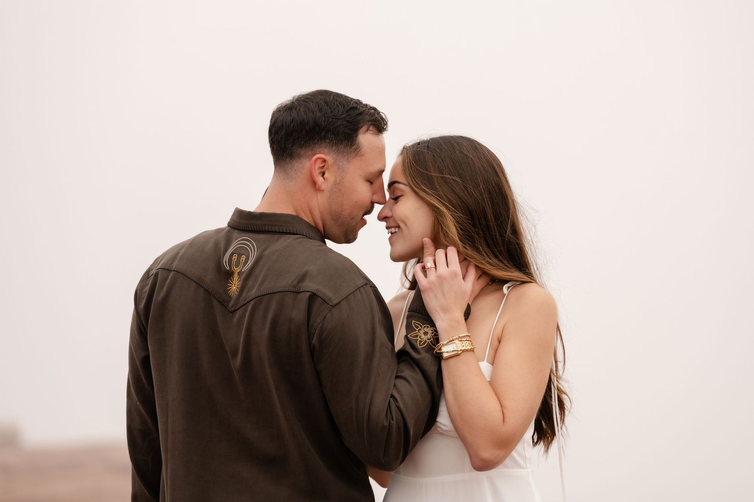 A couple embraces intimately against a white studio backdrop in warm earth-toned clothing.