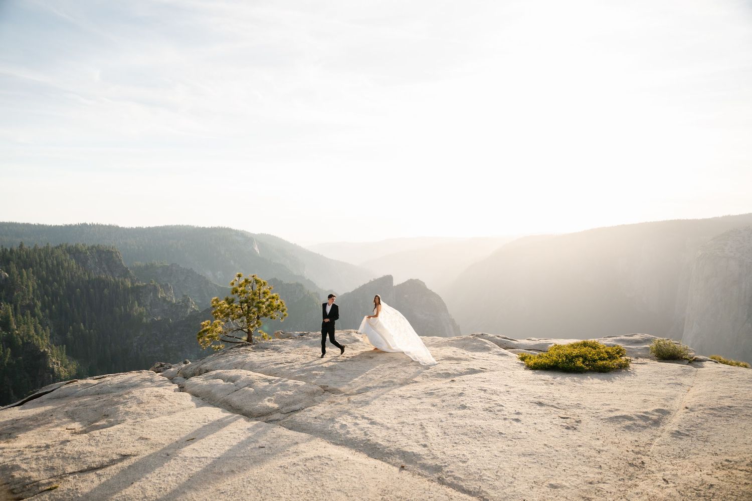 Wedding couple walking on granite overlook at Yosemite with sweeping valley and misty mountain views.