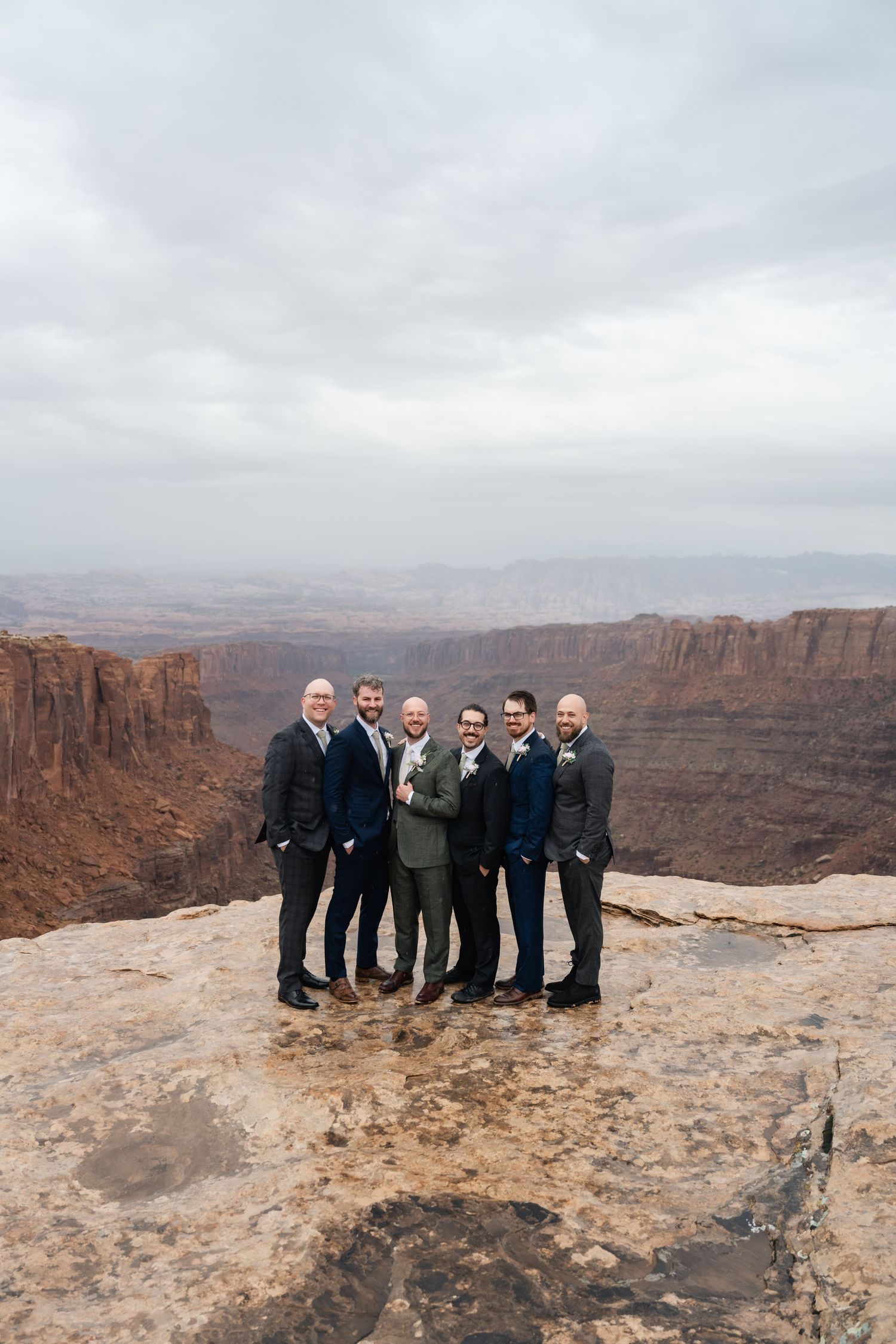 Wedding party members stand together on a rocky overlook with dramatic canyon views in the background.