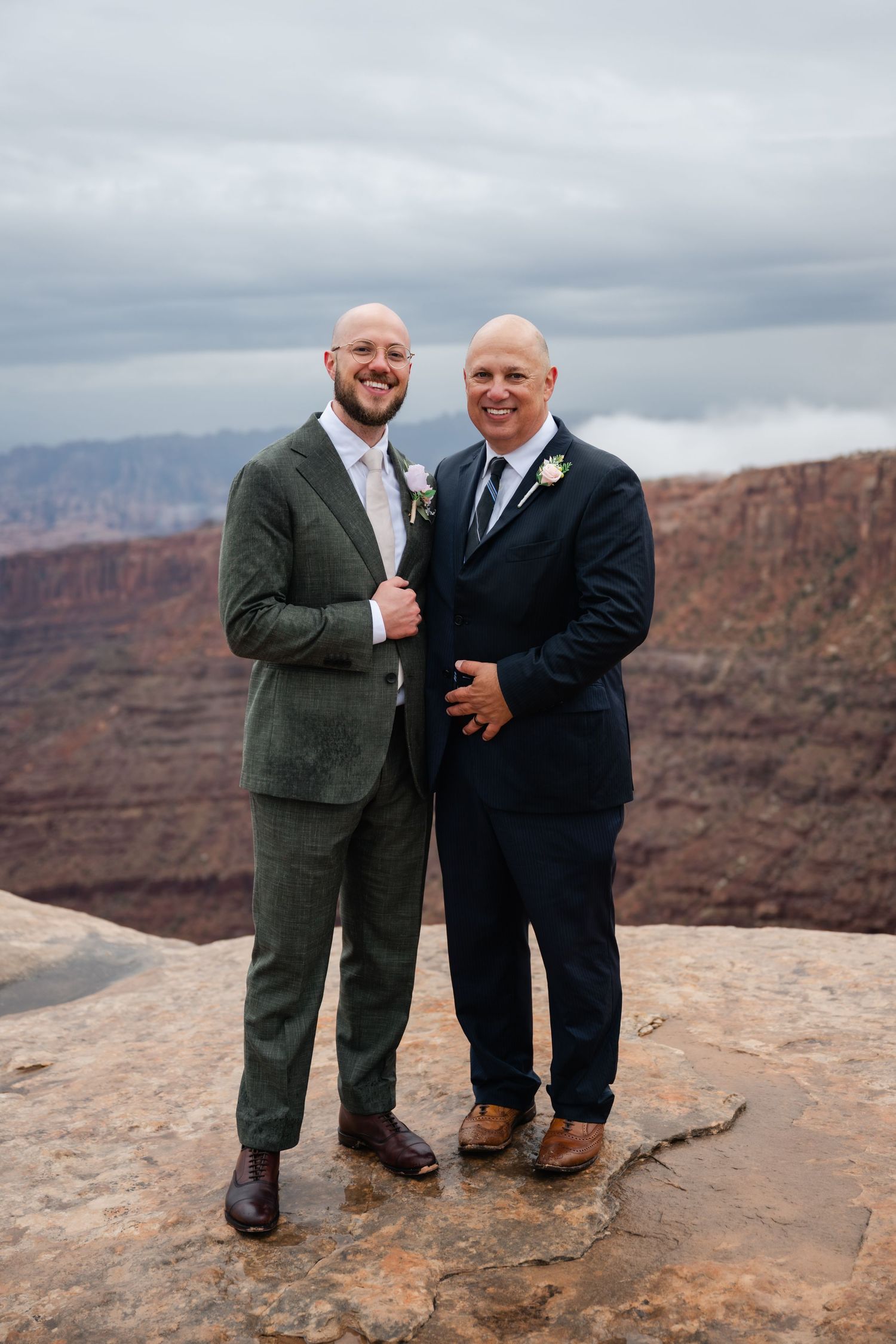 Two people in formal attire share a joyful moment at the edge of a scenic canyon overlook.