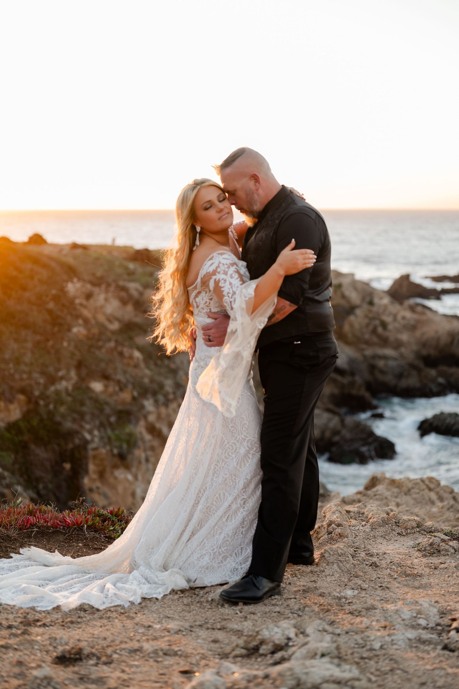 Sunset wedding photos on rocky coastal cliffs with ocean waves crashing in the background.
