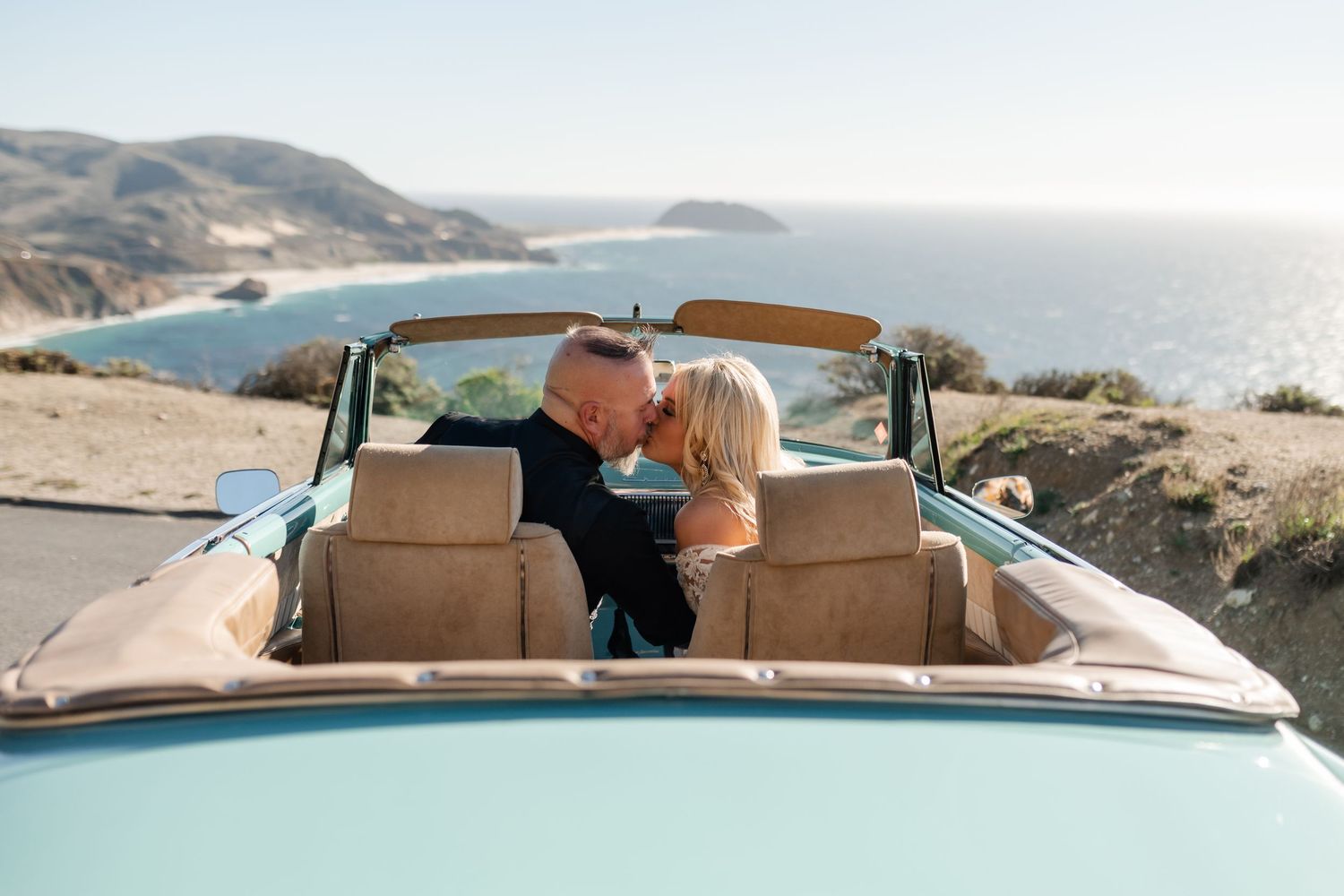 Vintage convertible car parked on scenic coastal cliff overlooking ocean at sunset.