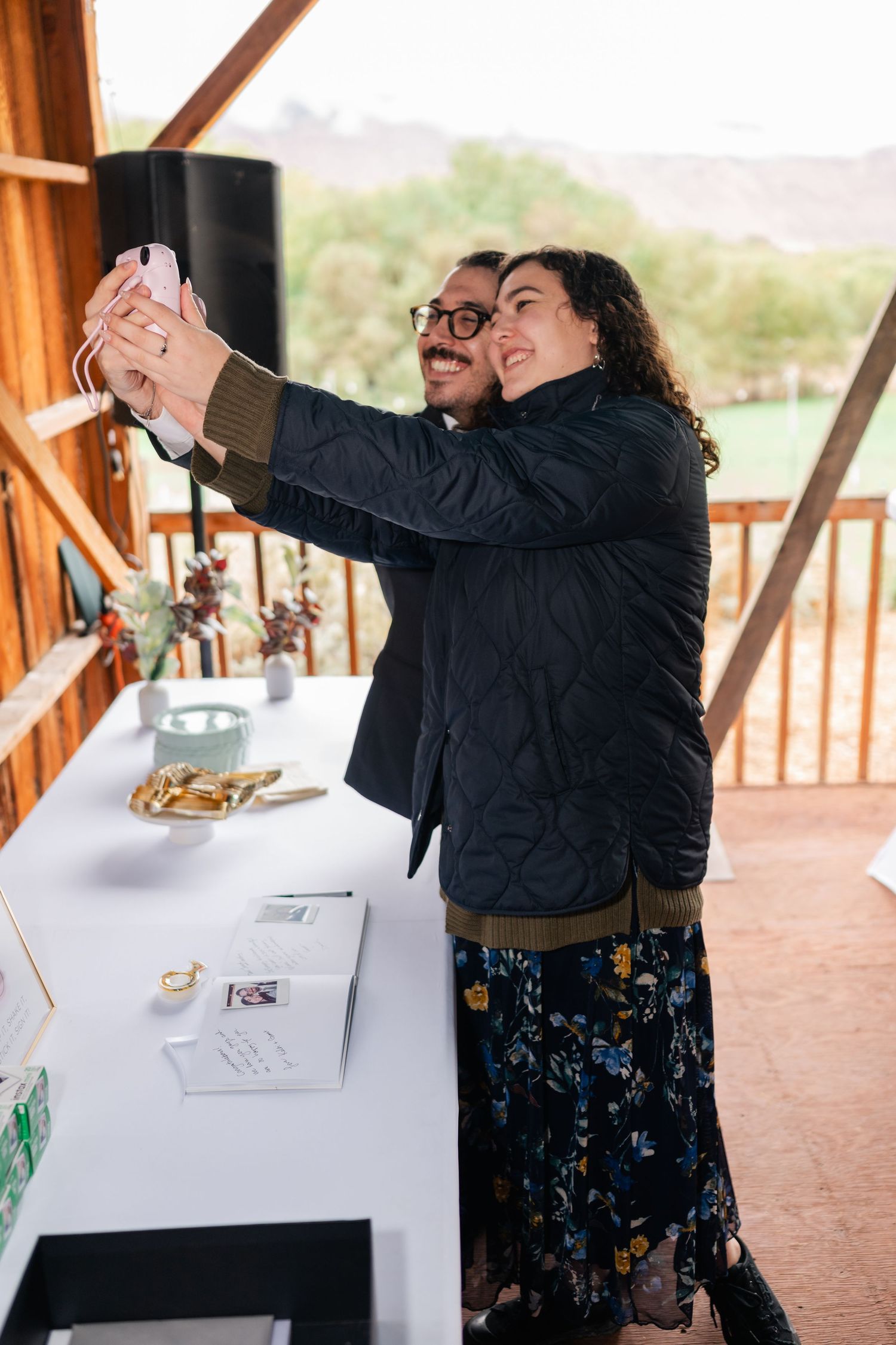 Two people taking a selfie together at an outdoor event with mountains visible in the background.