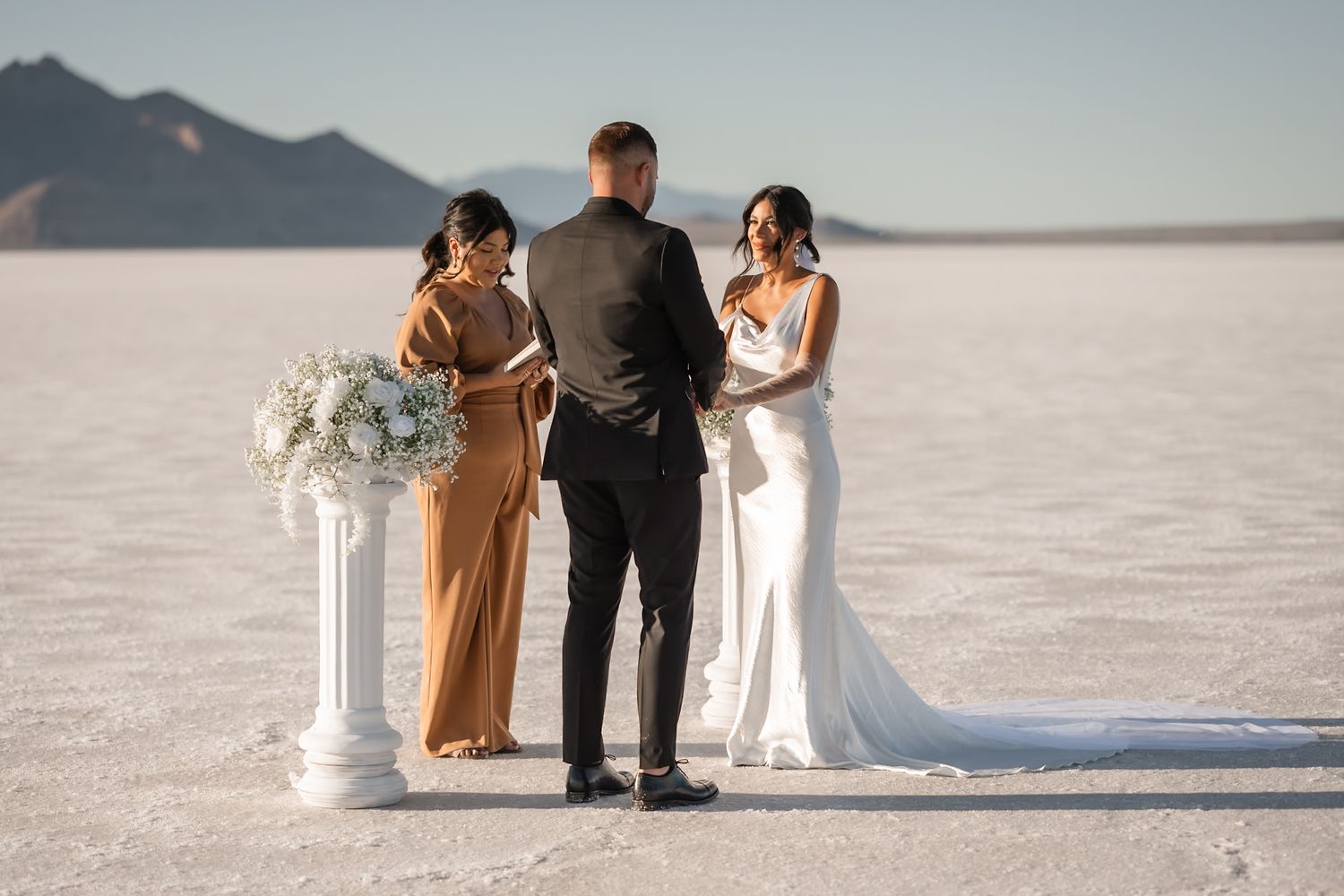 Small wedding gathering on salt flats with mountains in background.