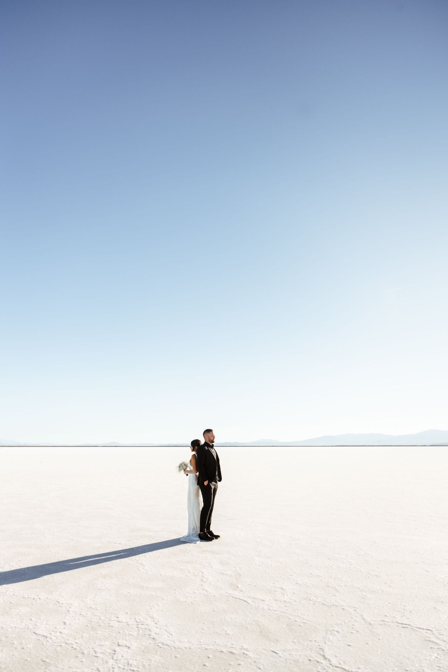 Minimalist wedding photography on vast salt flats under clear blue sky.