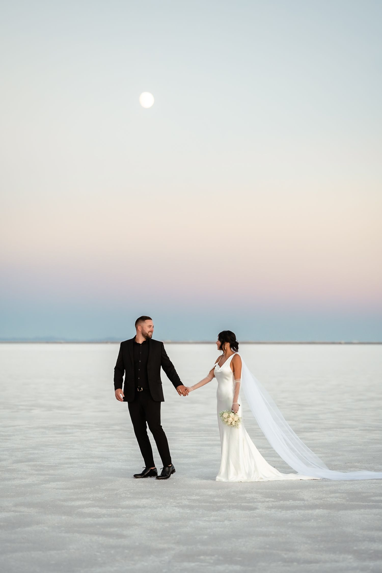 Romantic wedding photos on salt flats with couple walking and posing against pastel sky.