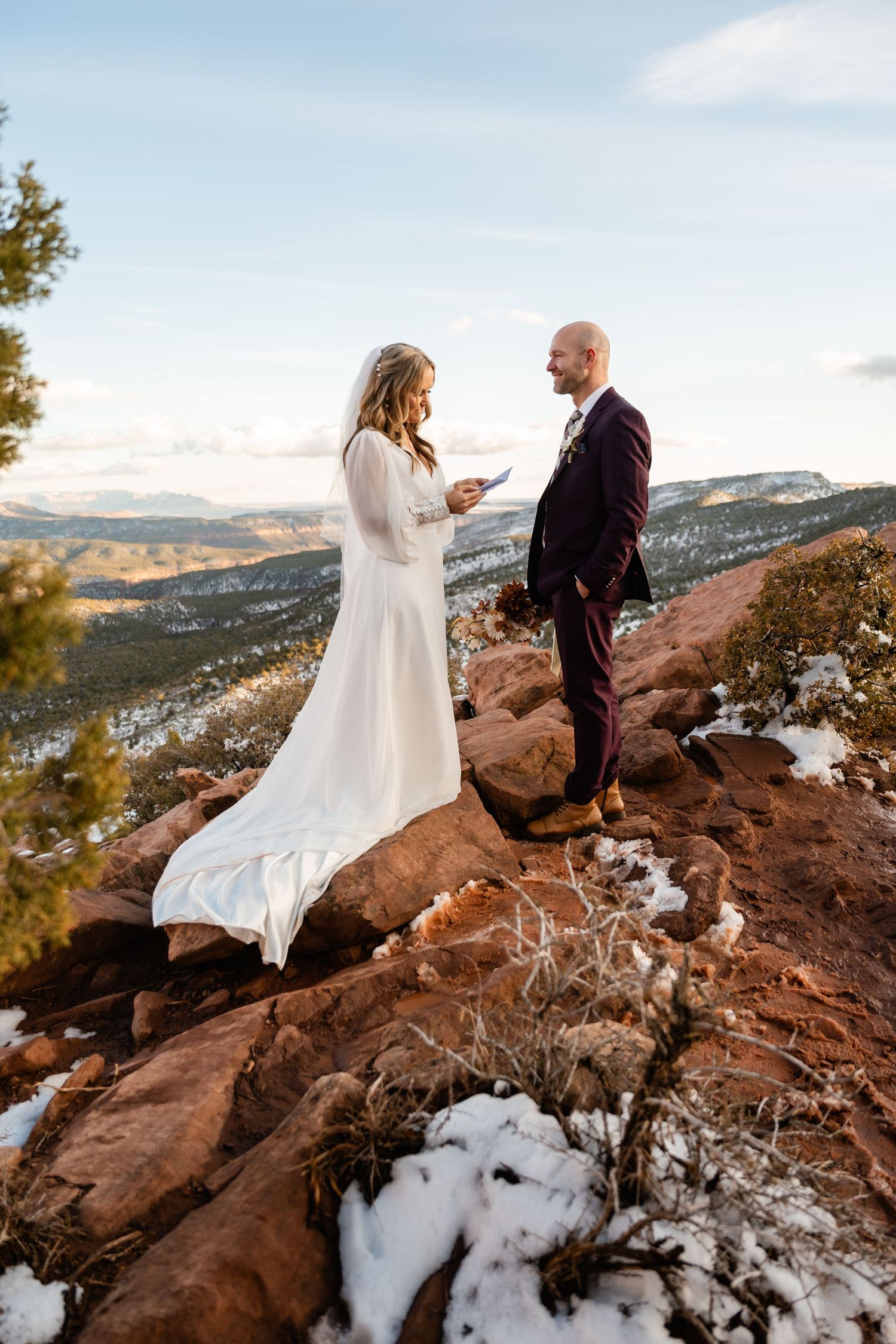 Wedding ceremony on snowy red rock cliff with dramatic mountain landscape backdrop.