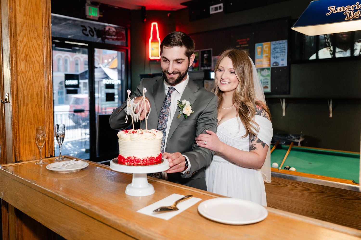 A couple shares their wedding cake together at a bar counter during their casual reception.