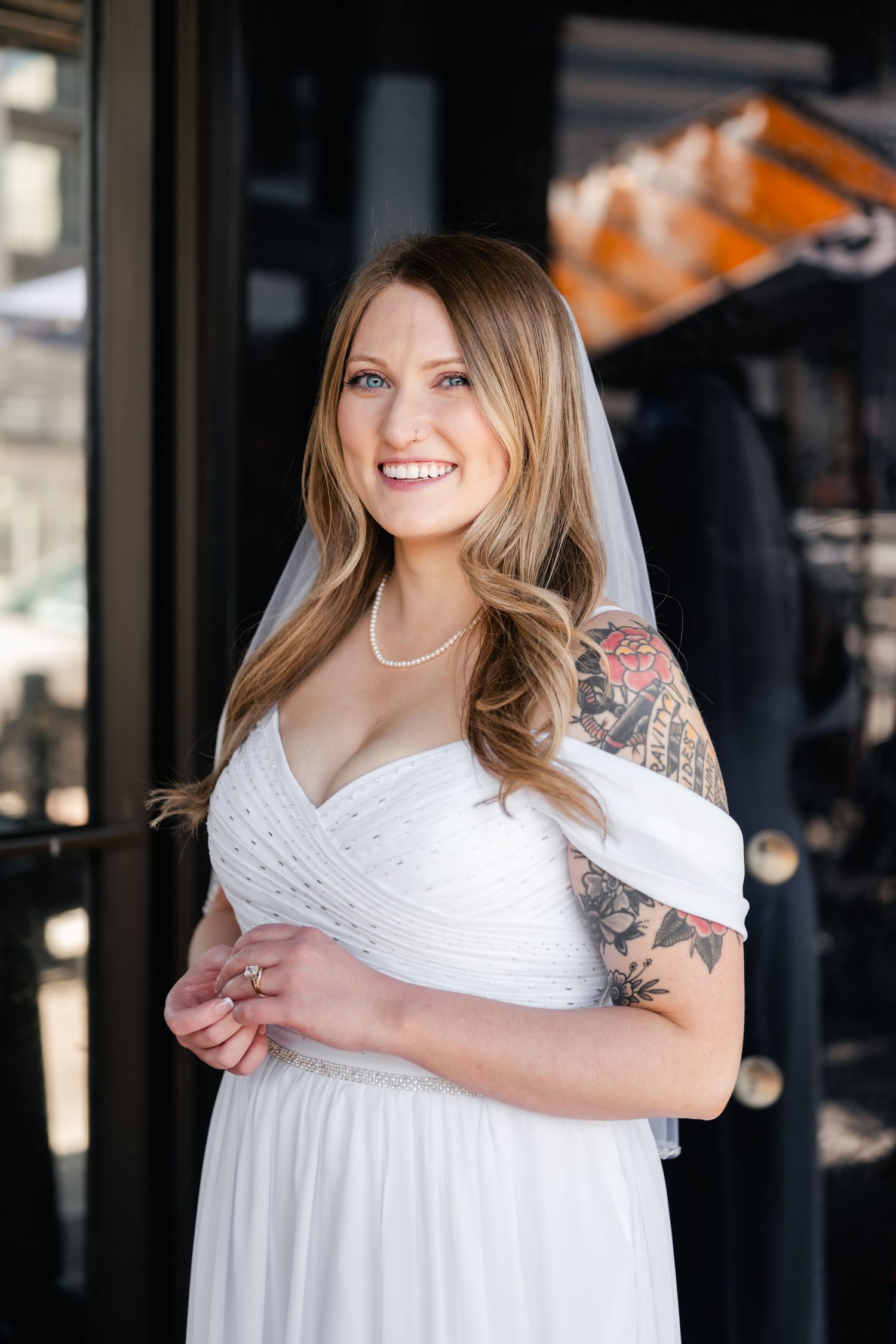 Bride in white empire waist dress with short sleeves and tattoos poses indoors.